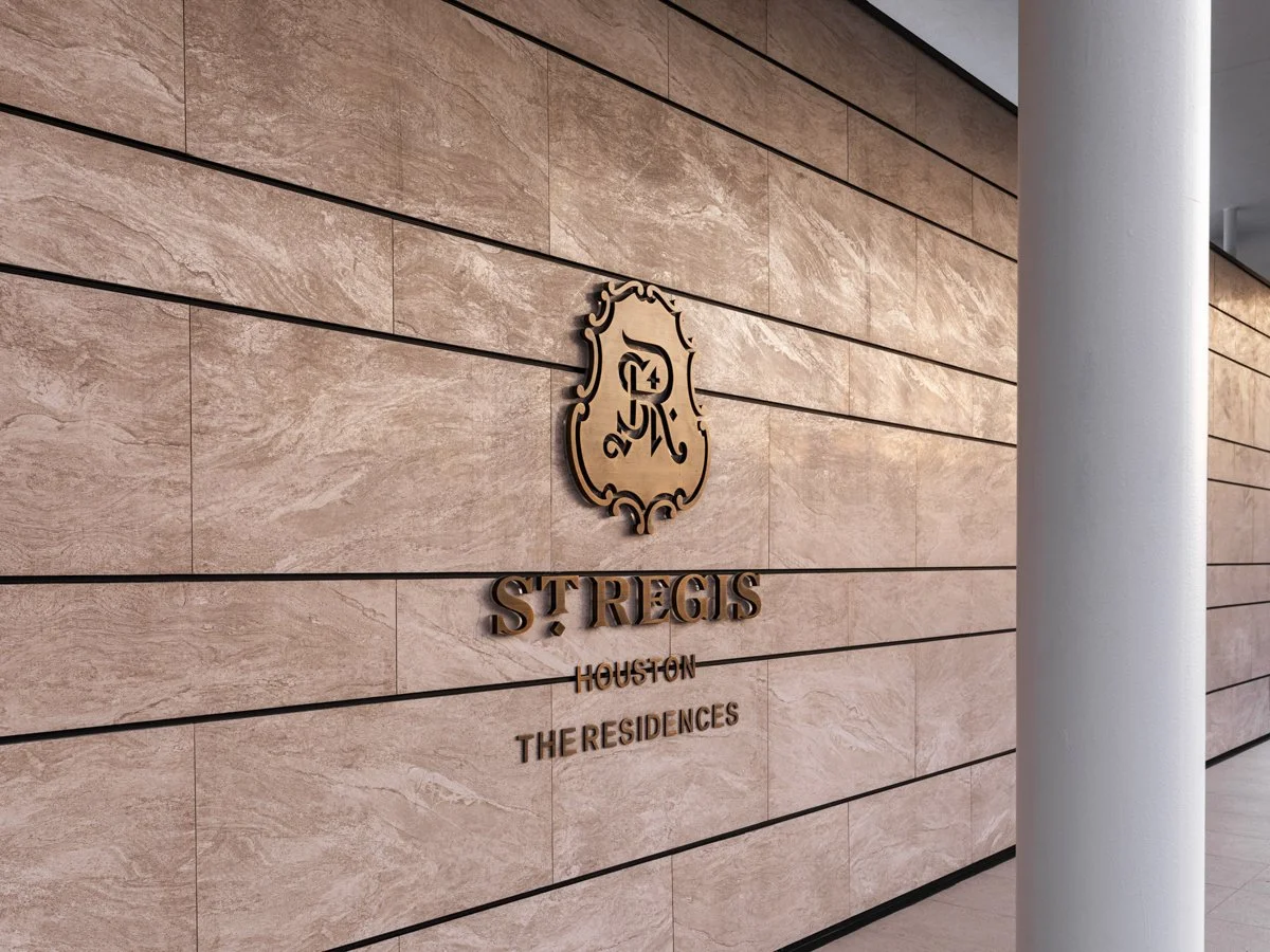 Sign on a beige stone wall reading 'St Regis Houston The Residences' with a crest emblem featuring an 'S' and a fleur-de-lis.