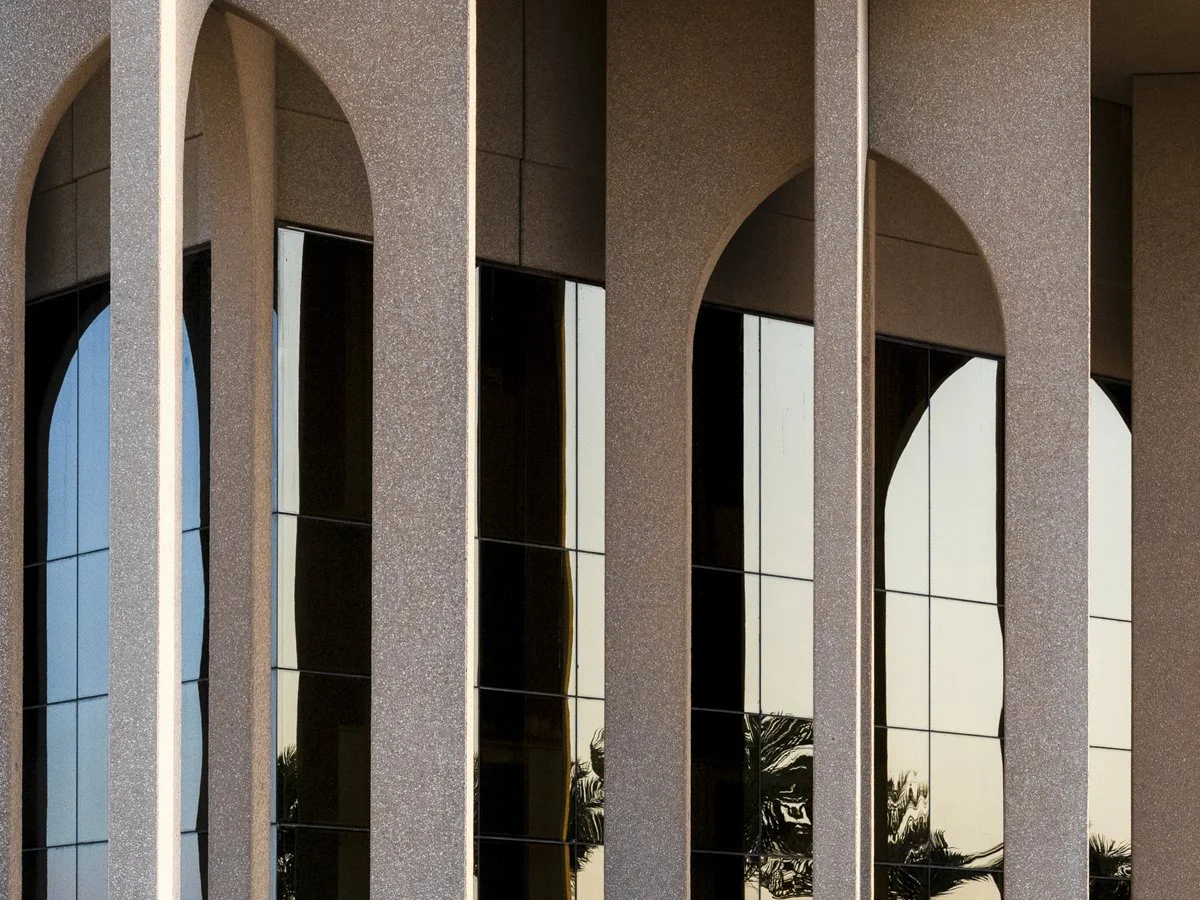 Reflection of palm trees in the glass windows of a modern building with arched architectural features.