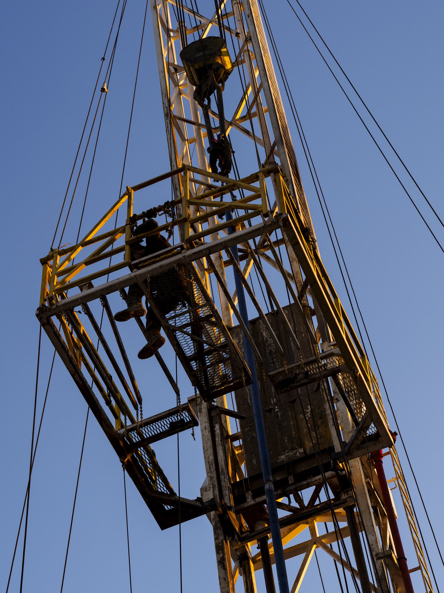 Workers climbing and working on a tall construction or telecommunications tower during sunset or dawn.
