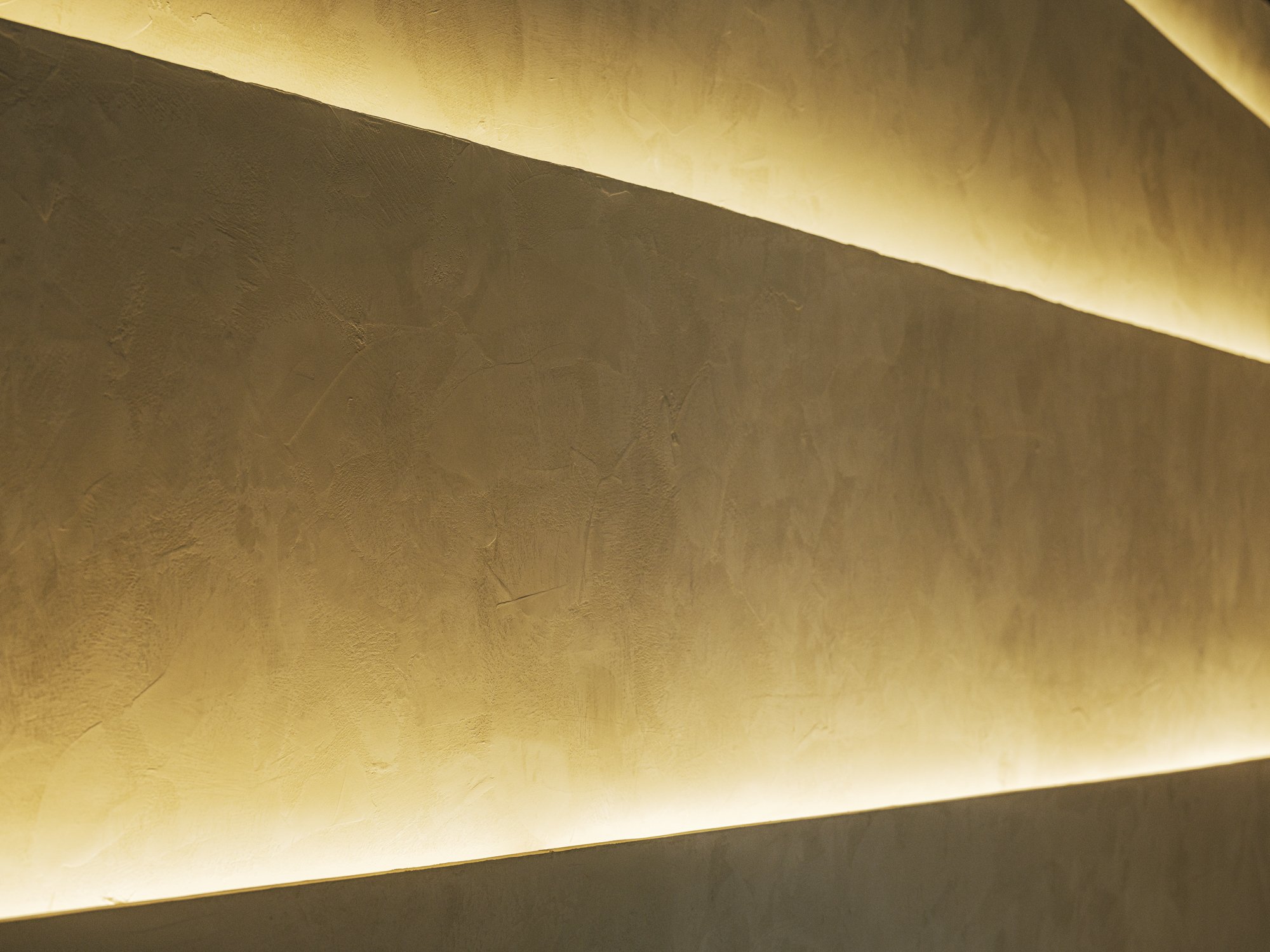 Close-up of a textured beige wall with indirect warm lighting creating a soft glow.