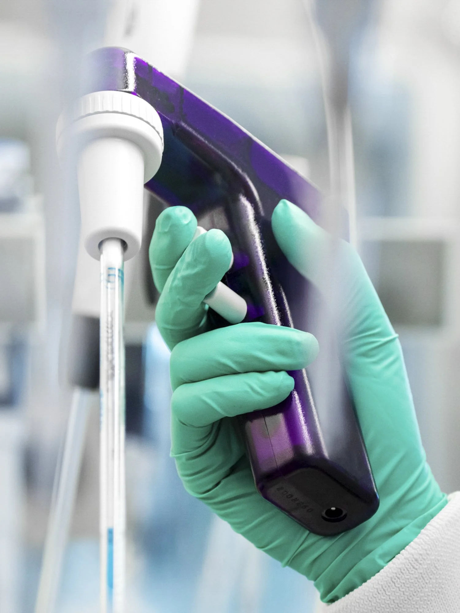 A person wearing green gloves holding a handheld infrared thermometer in a laboratory or medical setting.