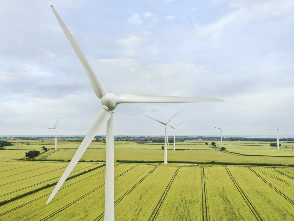 Wind turbines on a green farmland with fields and a cloudy sky.