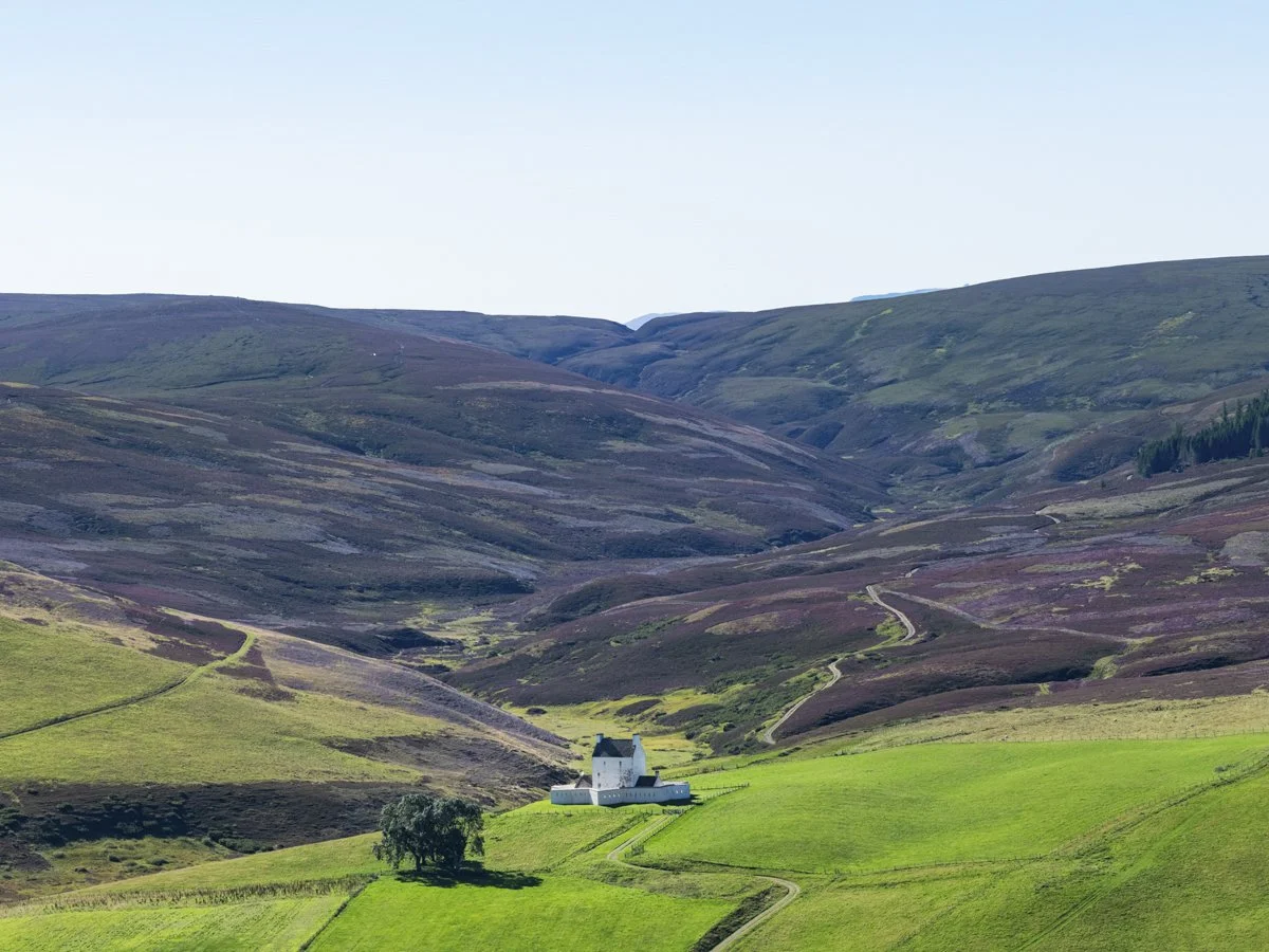 A mountain landscape with green hills, a small white church with a dark roof, and winding dirt roads.
