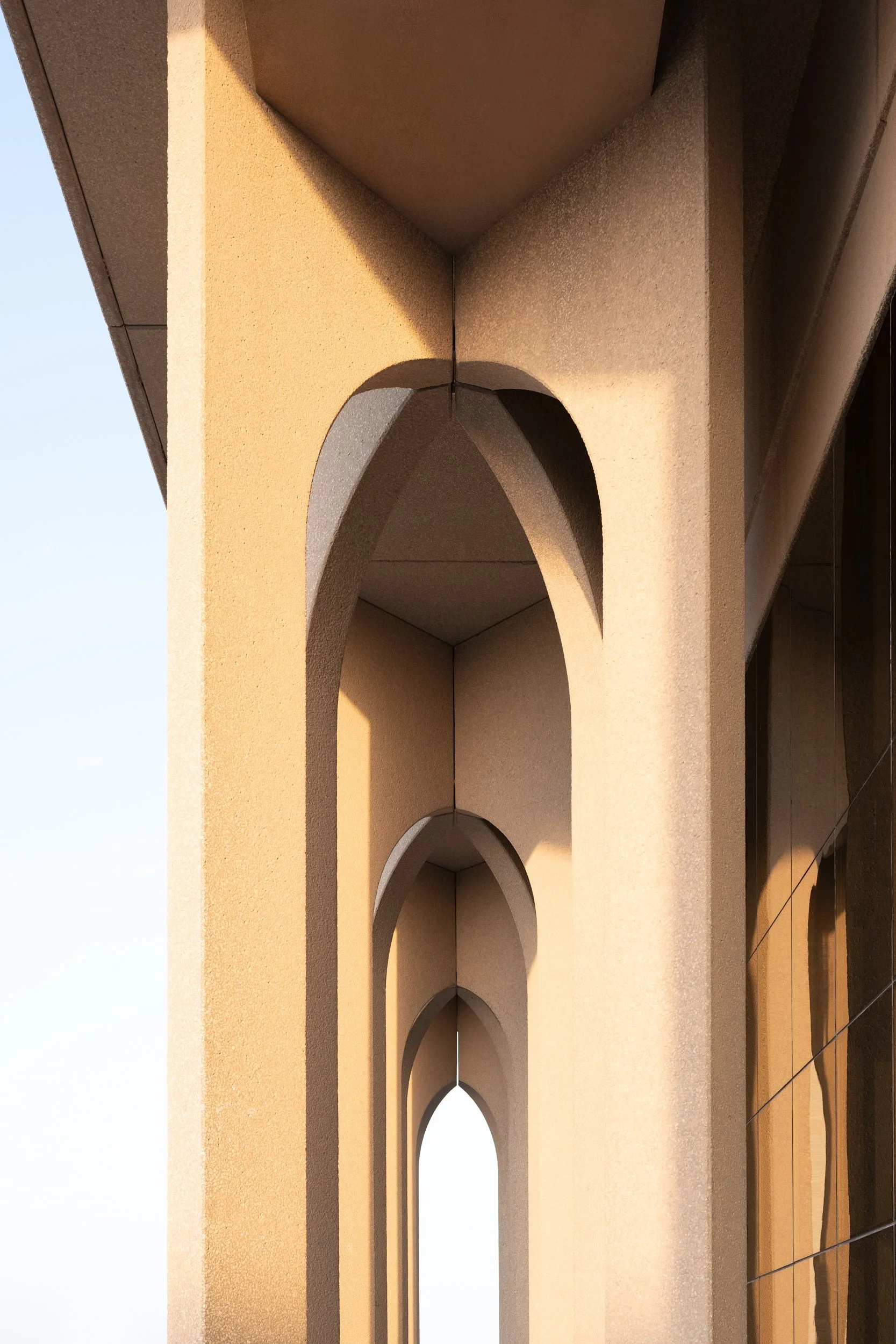 Close-up of an architectural detail on a building, featuring multiple arched openings and textured beige walls with sunlight casting shadows.