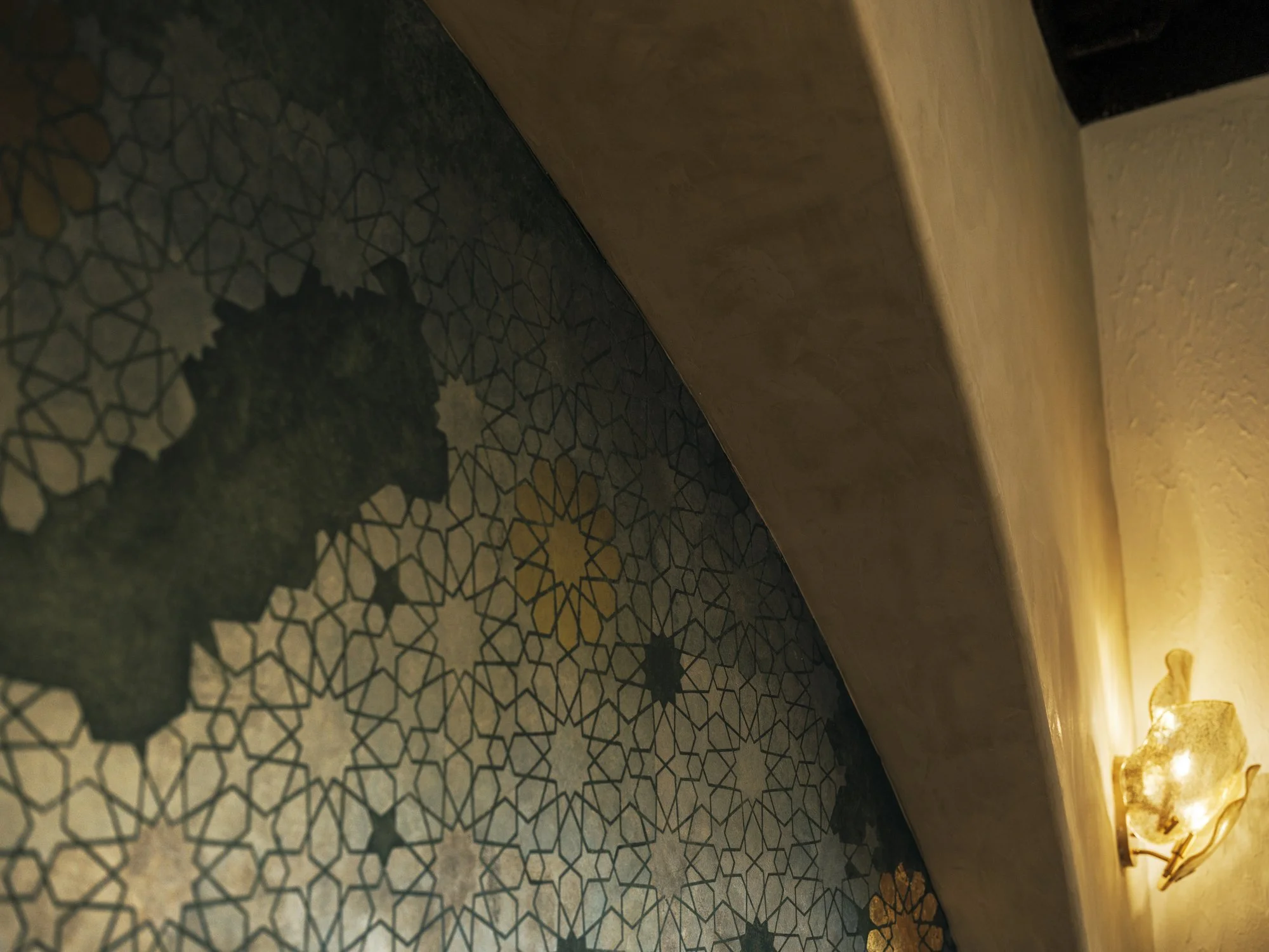 Close-up of a patterned floor with geometric shapes and a wall-mounted light fixture on a textured wall.