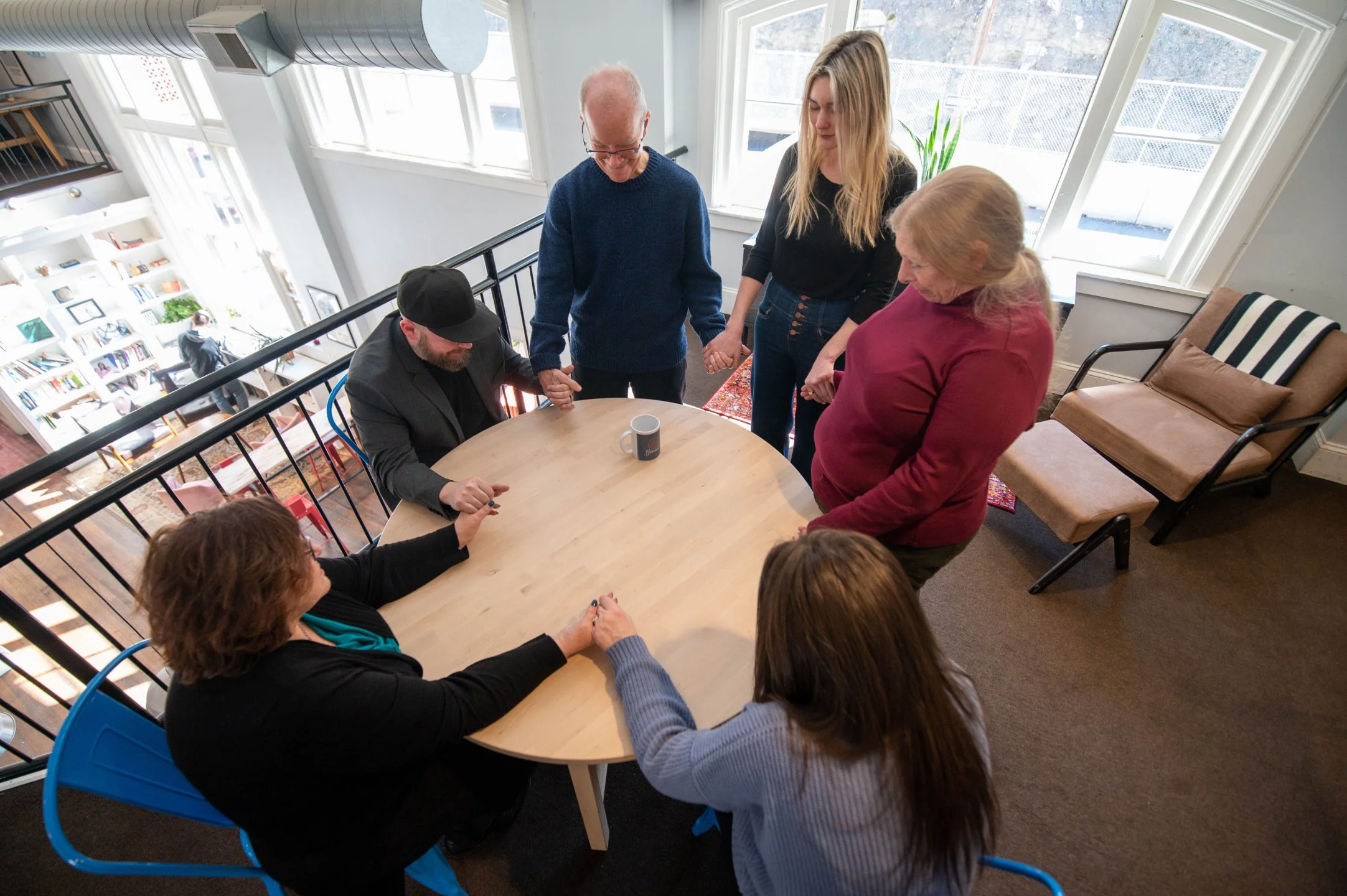Photo of a group led by Founder John Davies holding hands around a table.
