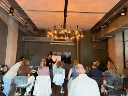Een groep mensen zit aan tafels in een vergaderruimte, terwijl iemand voor een scherm een presentatie geeft.