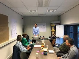 Man die een presentatie geeft in een vergaderruimte met vijf aanwezigen. Voorzitter lezing en stagesprint 