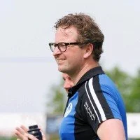 Man met bril en sportkleding, buiten in een groene omgeving.