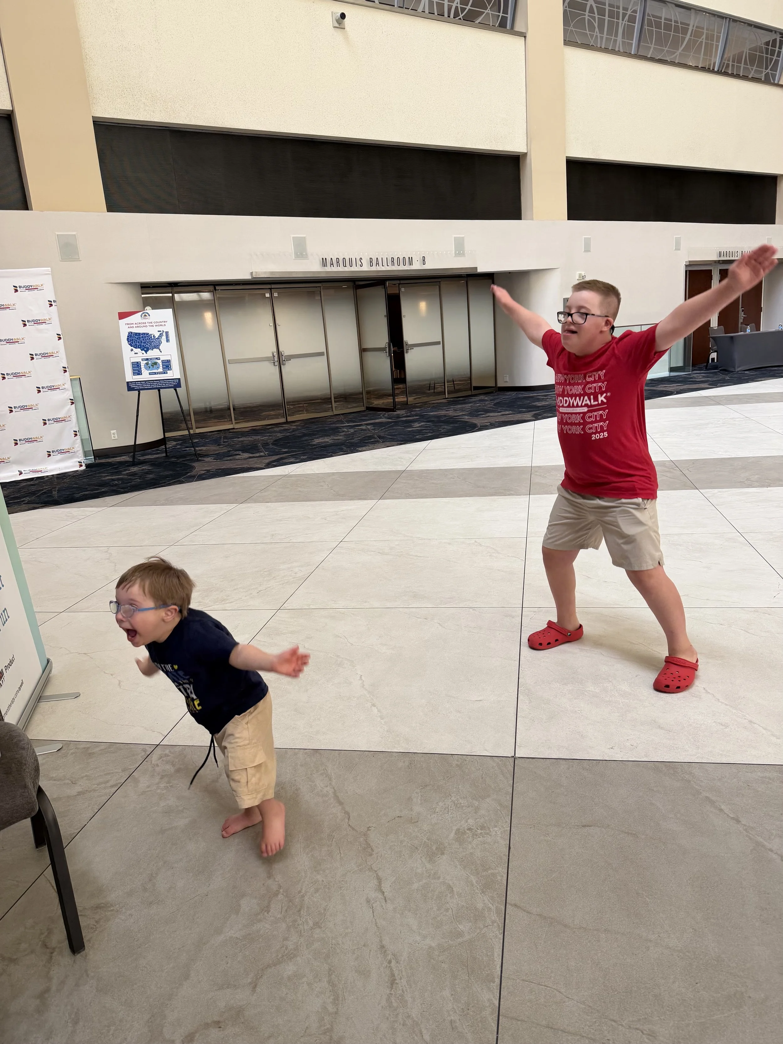 A young man plays ARWell with a very young child, both wearing glasses and having fun.