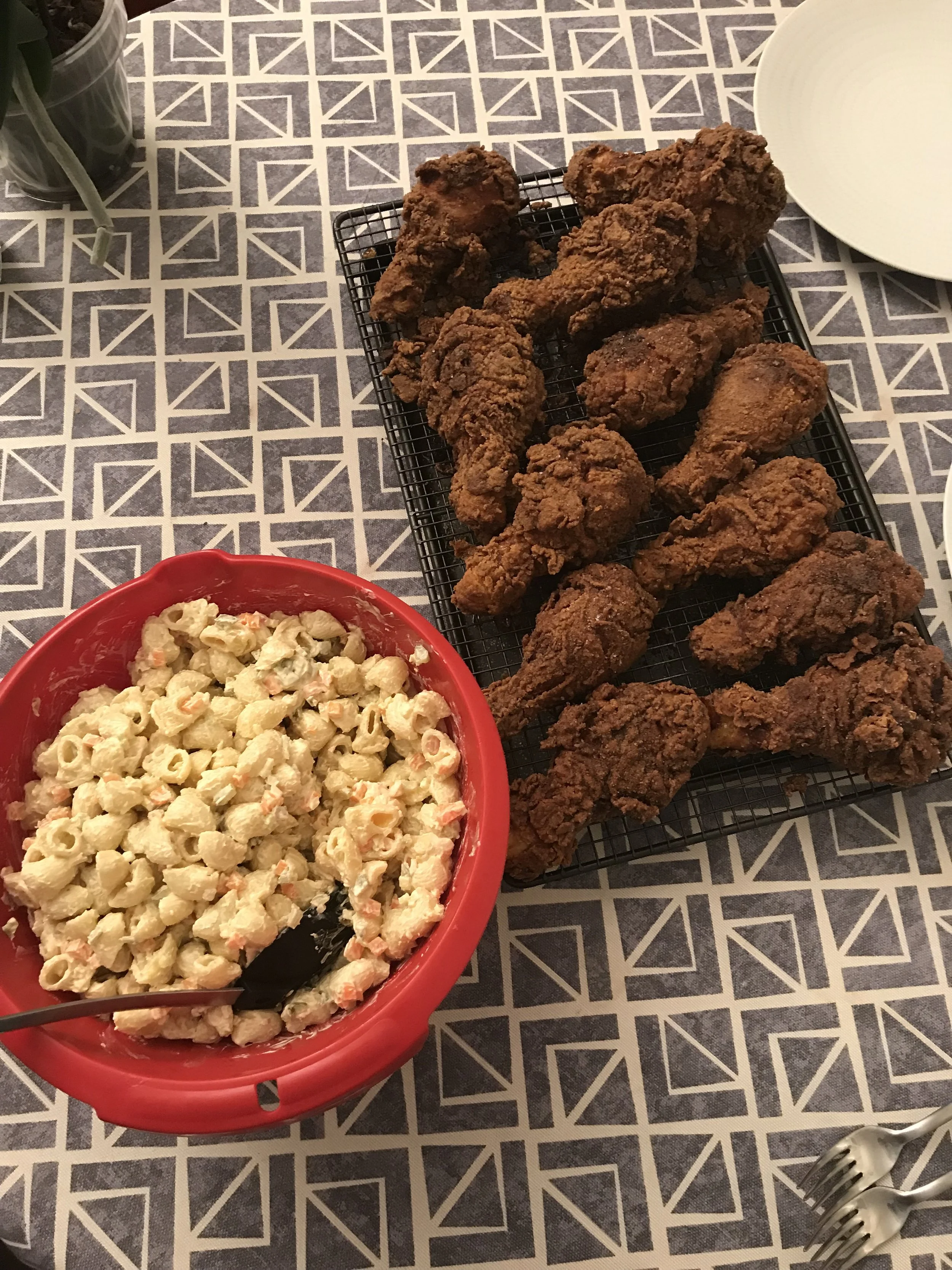 A tray of fried chicken and a bowl of pasta salad on a table with a patterned tablecloth