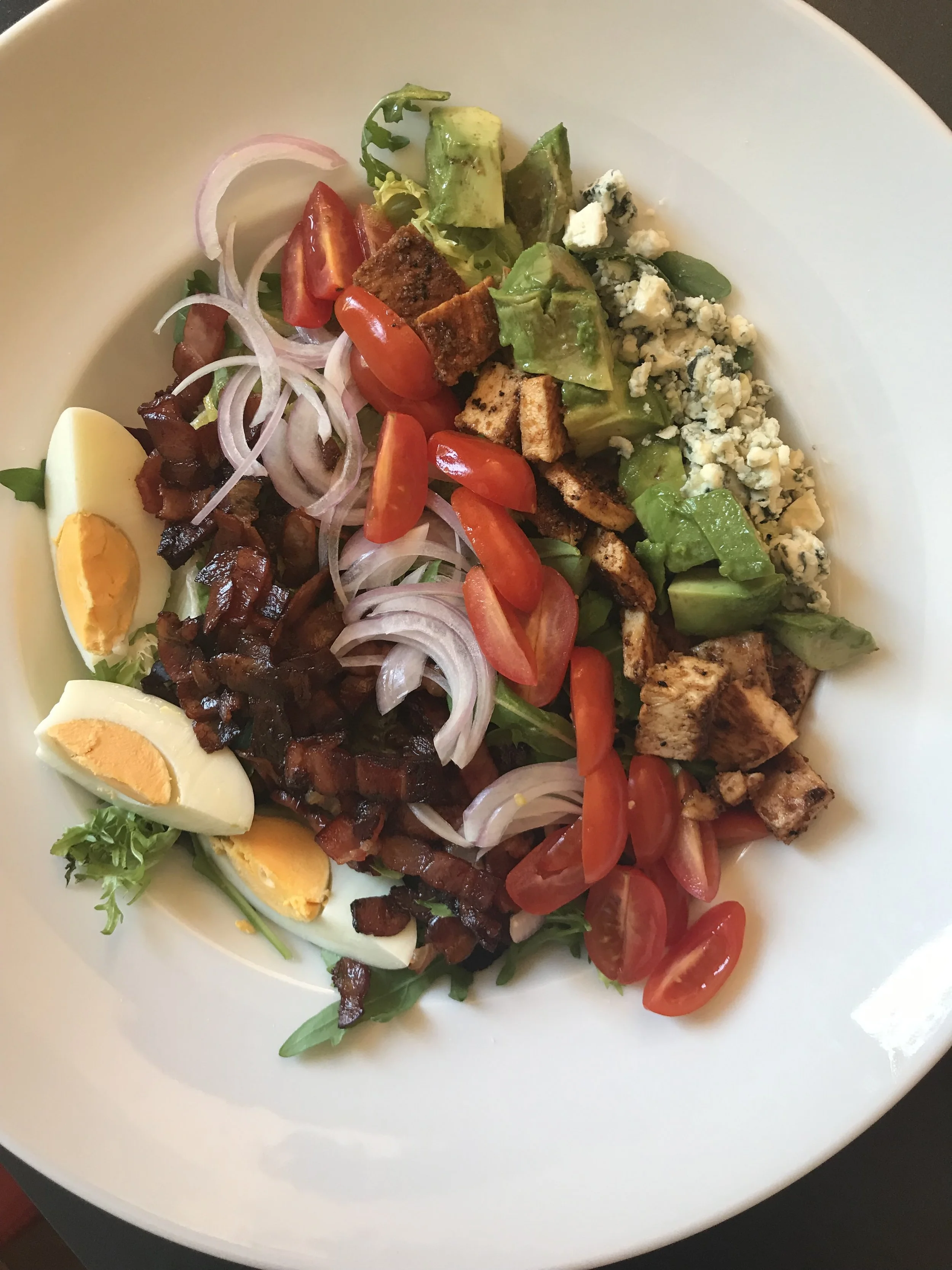 Cobb salad with rows of hard boiled egg, bacon, tomatoes, grilled chicken, avocado, and blue cheese