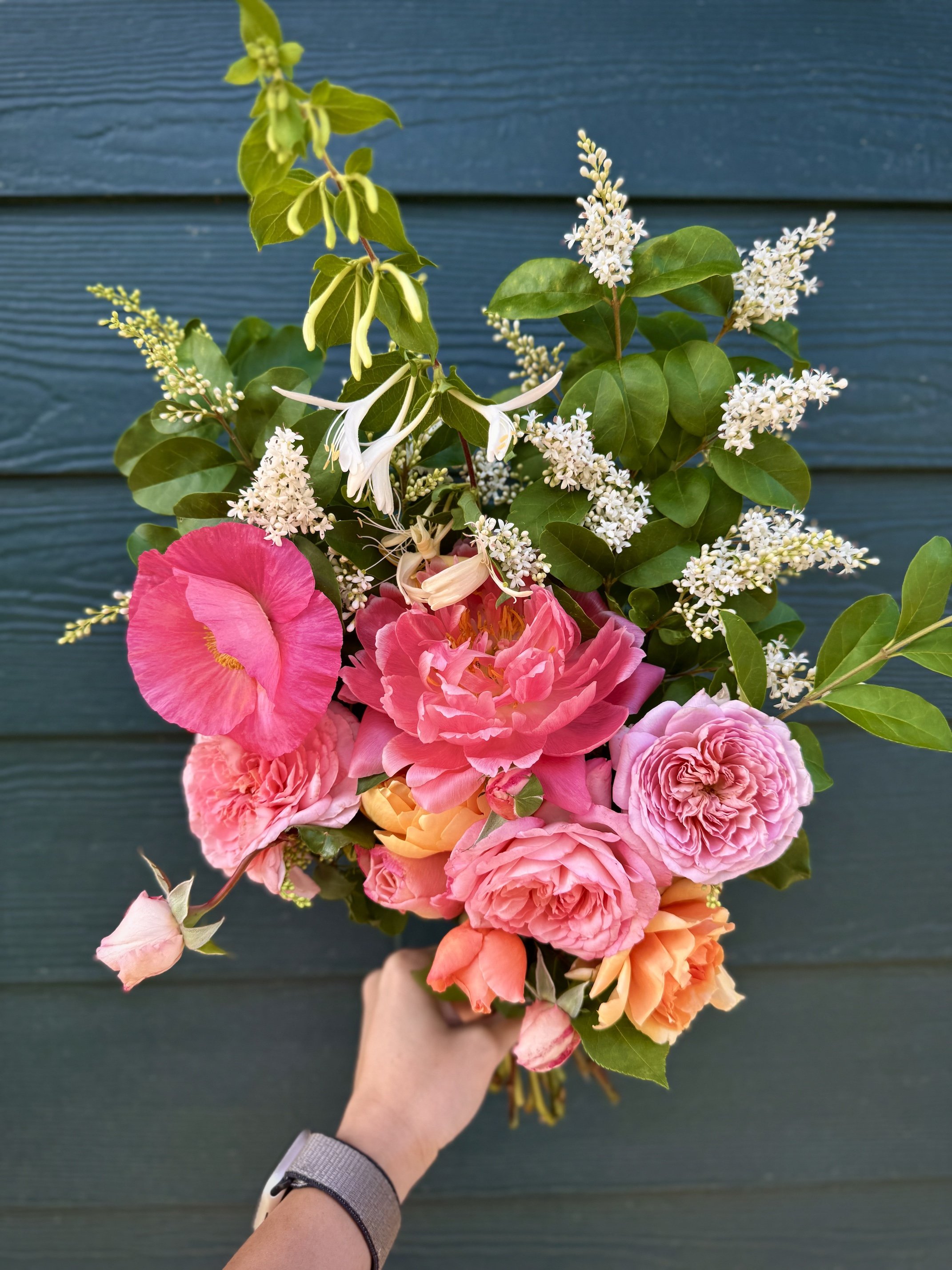 Handheld bouquet of roses, peonies, poppies, and honeysuckle in pinks and peaches