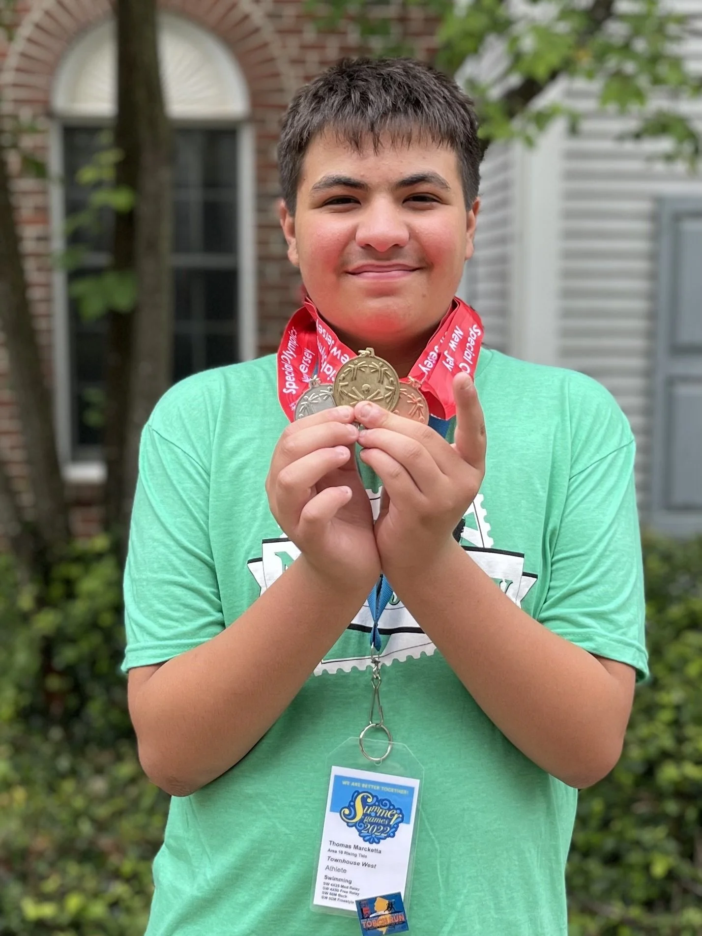 Teenage boy, Tommy, who is featured in this story, standing outside proudly holding his swim medals.
