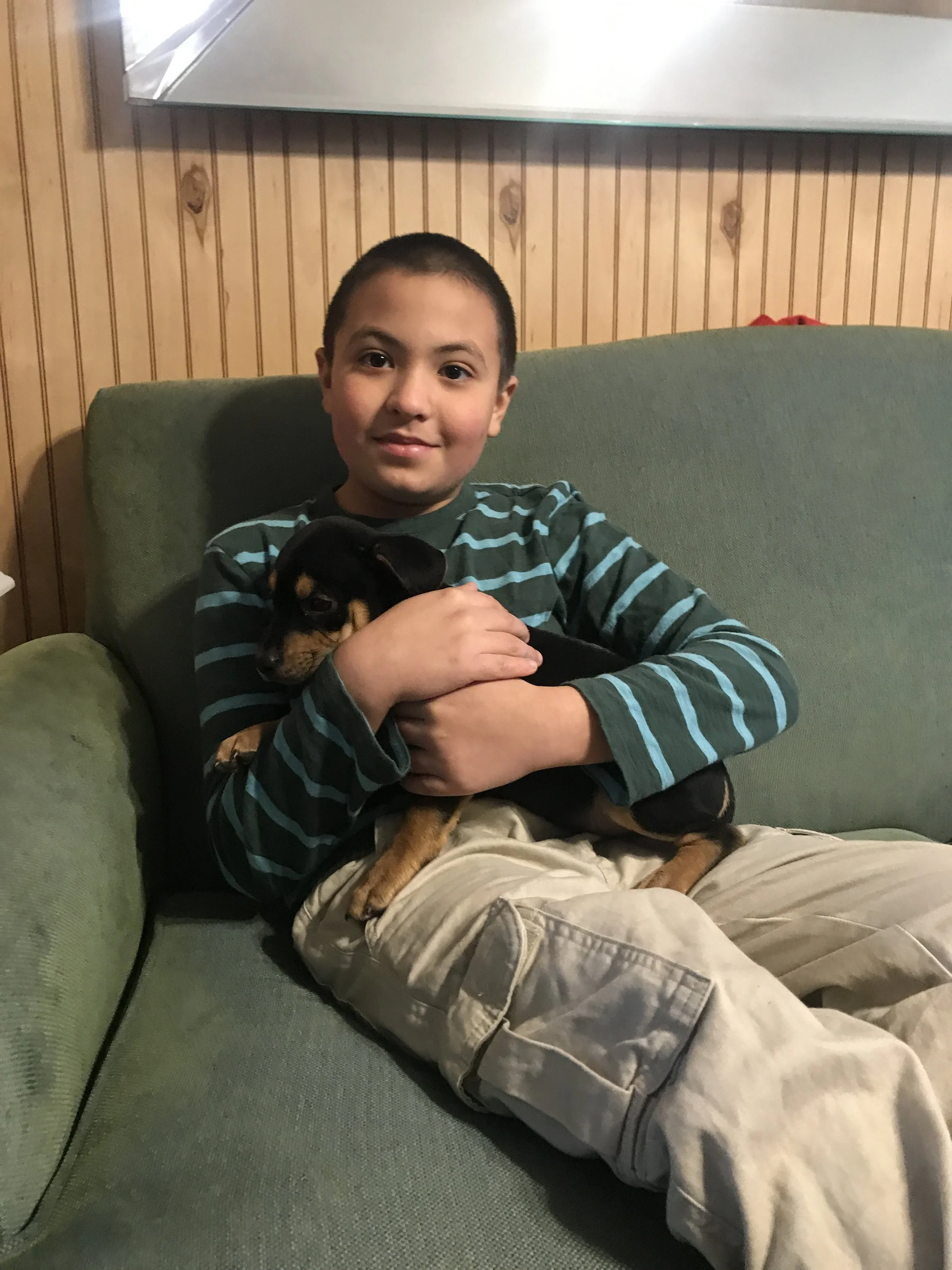 A young boy, Tommy who is featured in the story, sitting on a sofa, holding a puppy.