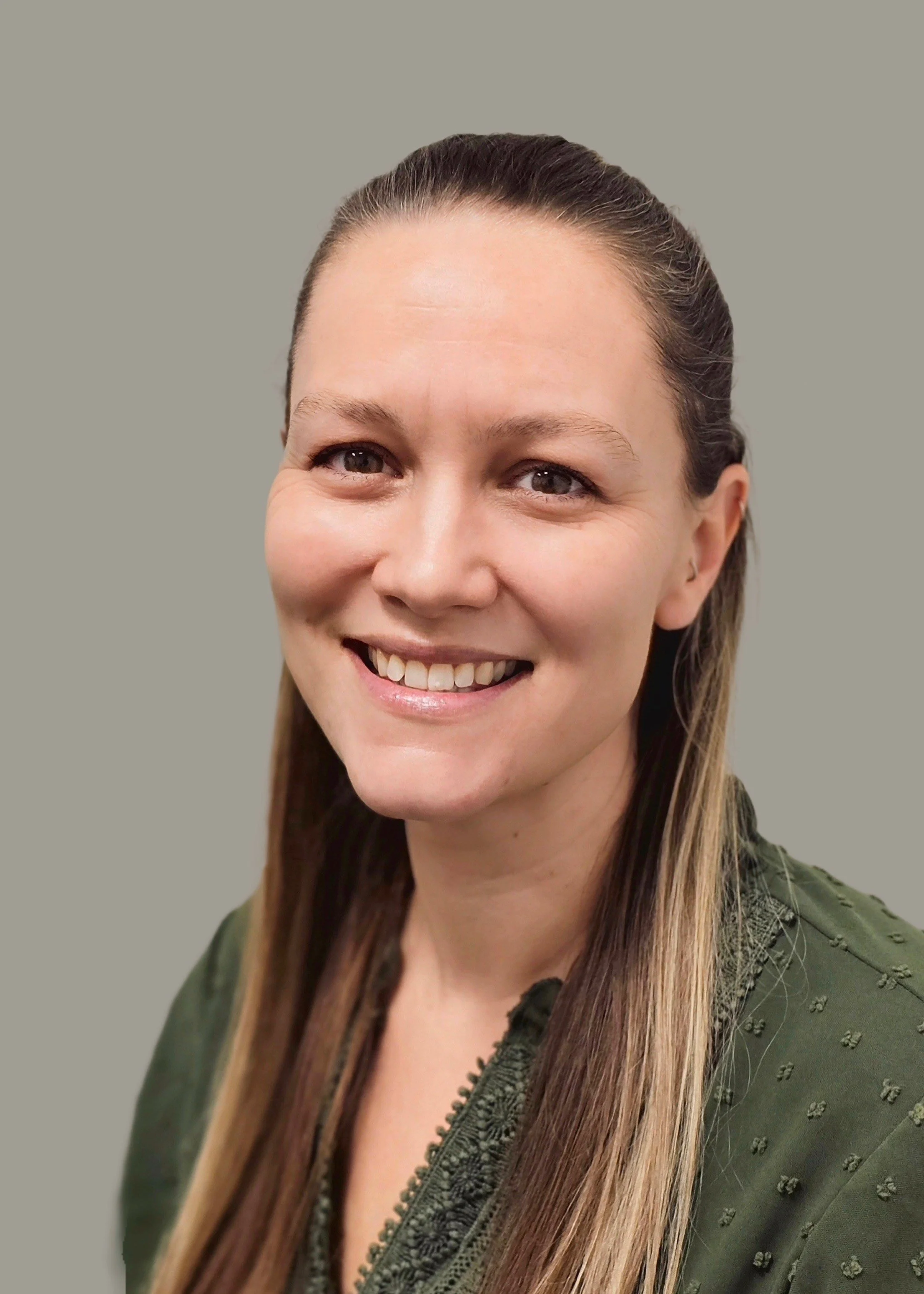 Close-up portrait of a smiling woman with long brown hair, wearing a green jacket, against a plain background.