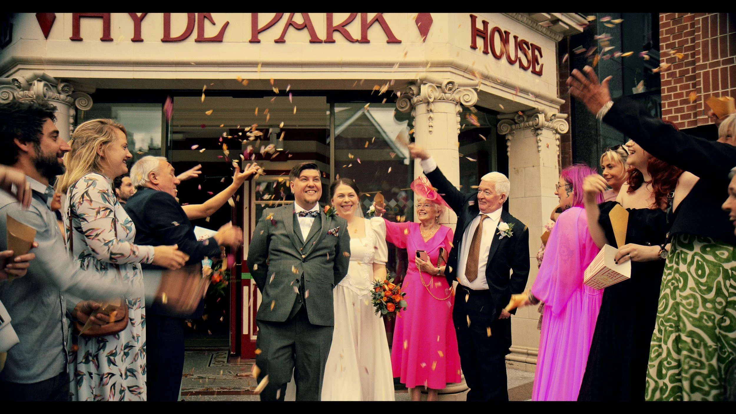 Wedding celebration outside a building called Hyde Park House, with guests throwing confetti and celebrating the newlyweds.