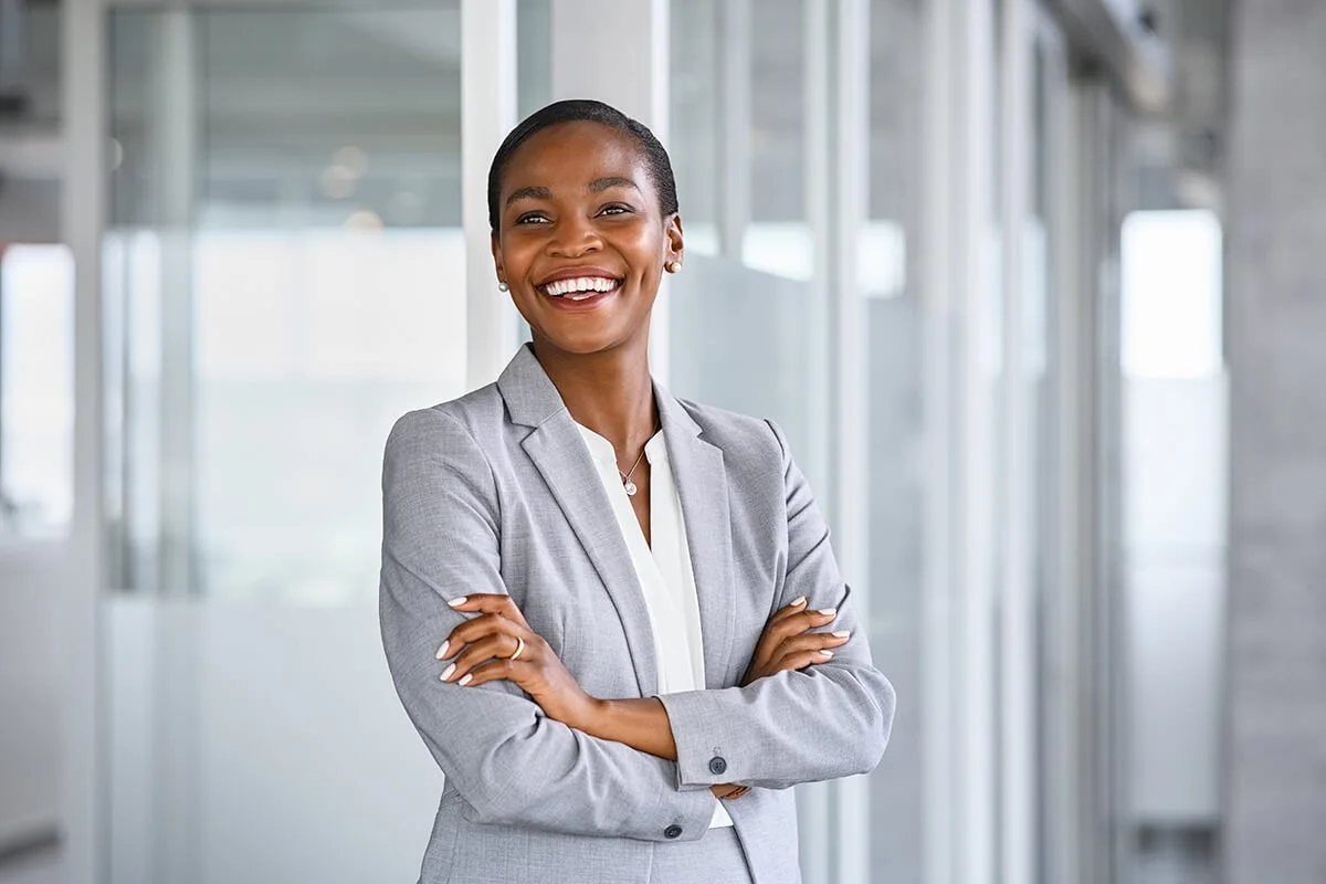 Une femme d'affaires souriante portant un costume gris dans un bureau moderne.