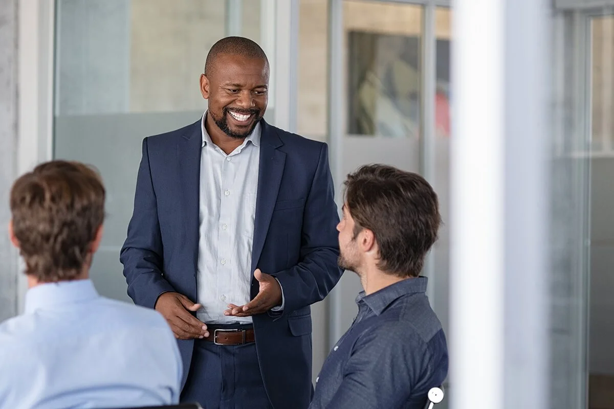 Un homme d'affaires souriant parle à deux autres hommes lors d'une réunion dans un bureau moderne.
