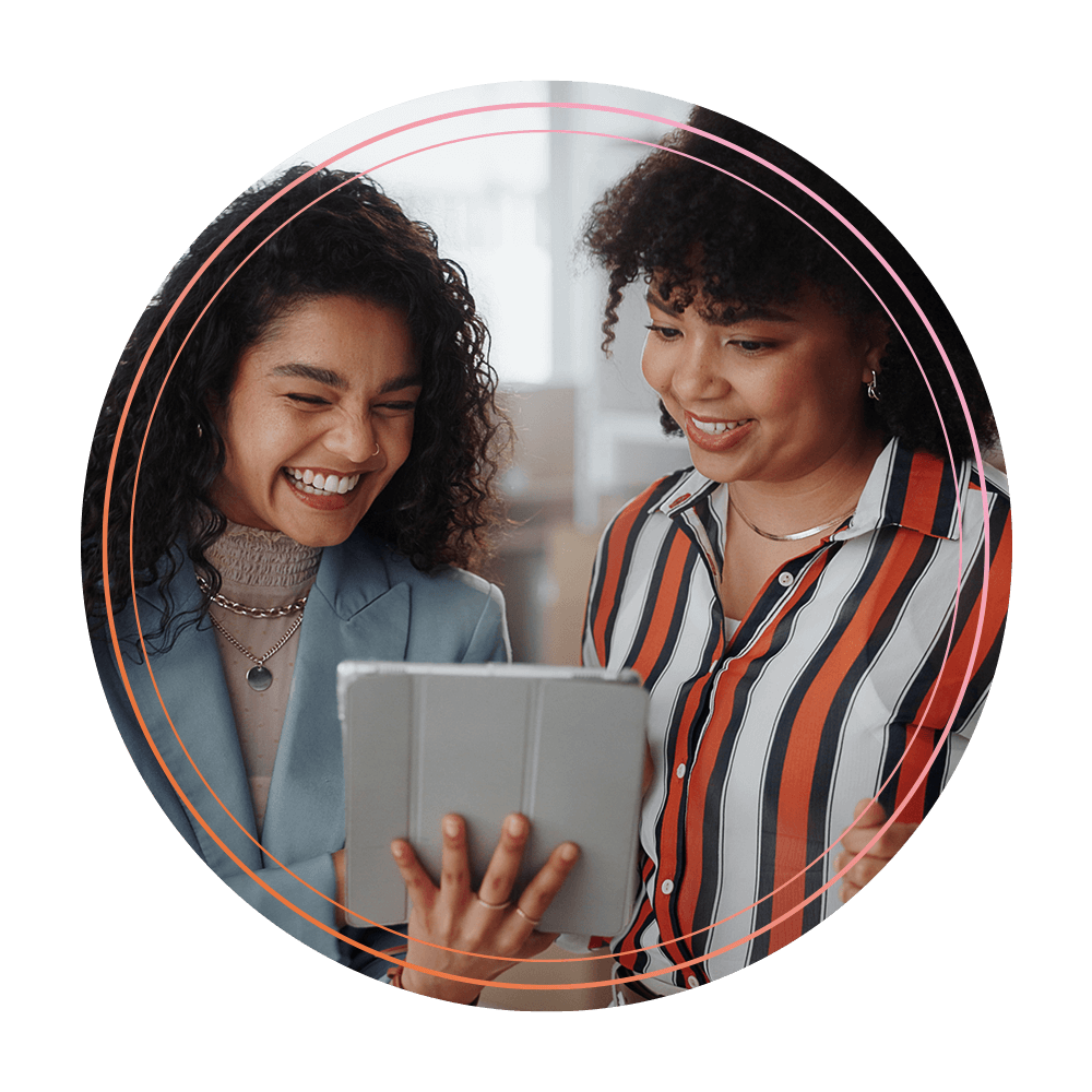 Deux femmes souriantes regardant une tablette ensemble dans un bureau lumineux.