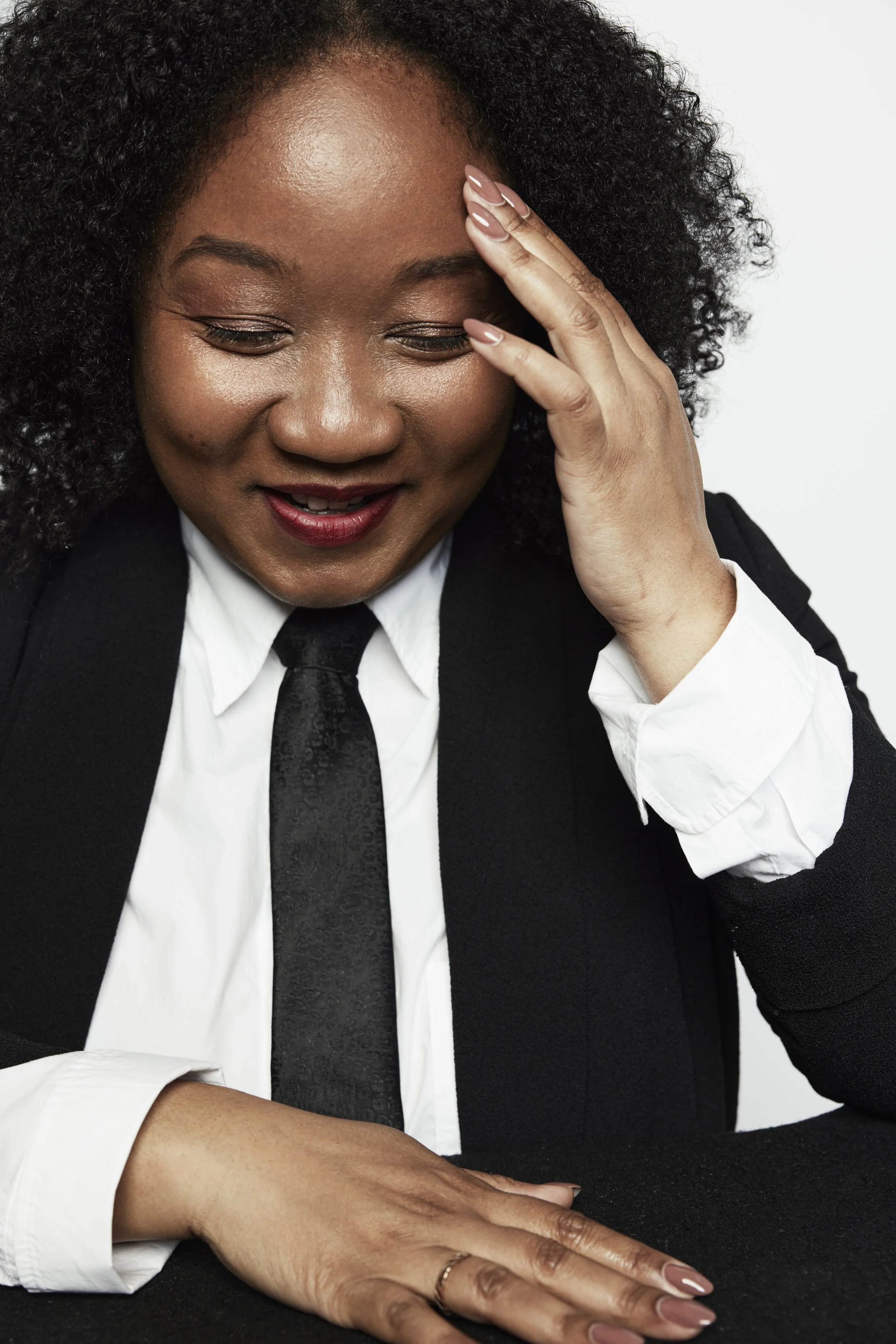 Coko Galore in a black suit, smiling with her hand at her temple
