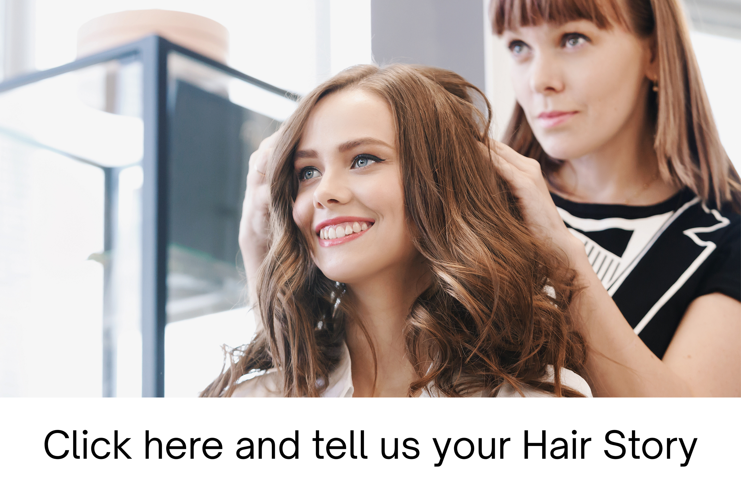 A hairstylist adjusting a woman's long, curly, auburn hair in a salon setting with natural light.