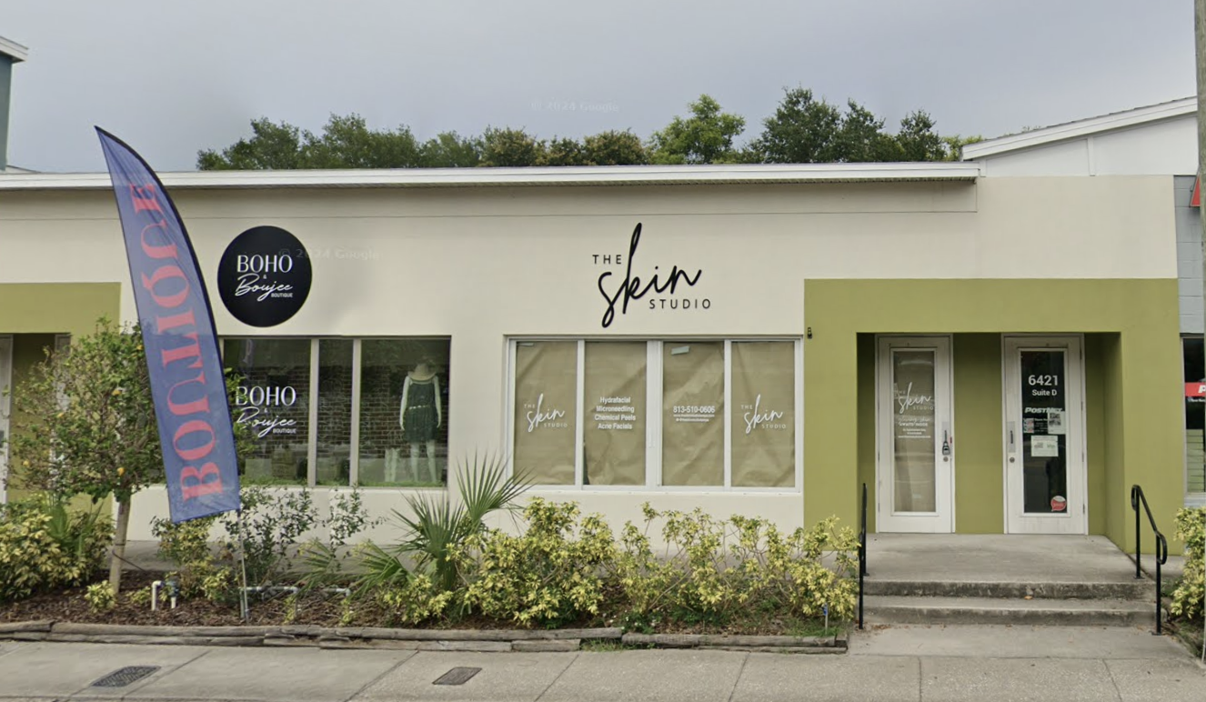 The storefront of The Skin Studio, a beauty salon, featuring large windows, signage, and a small garden area in front.