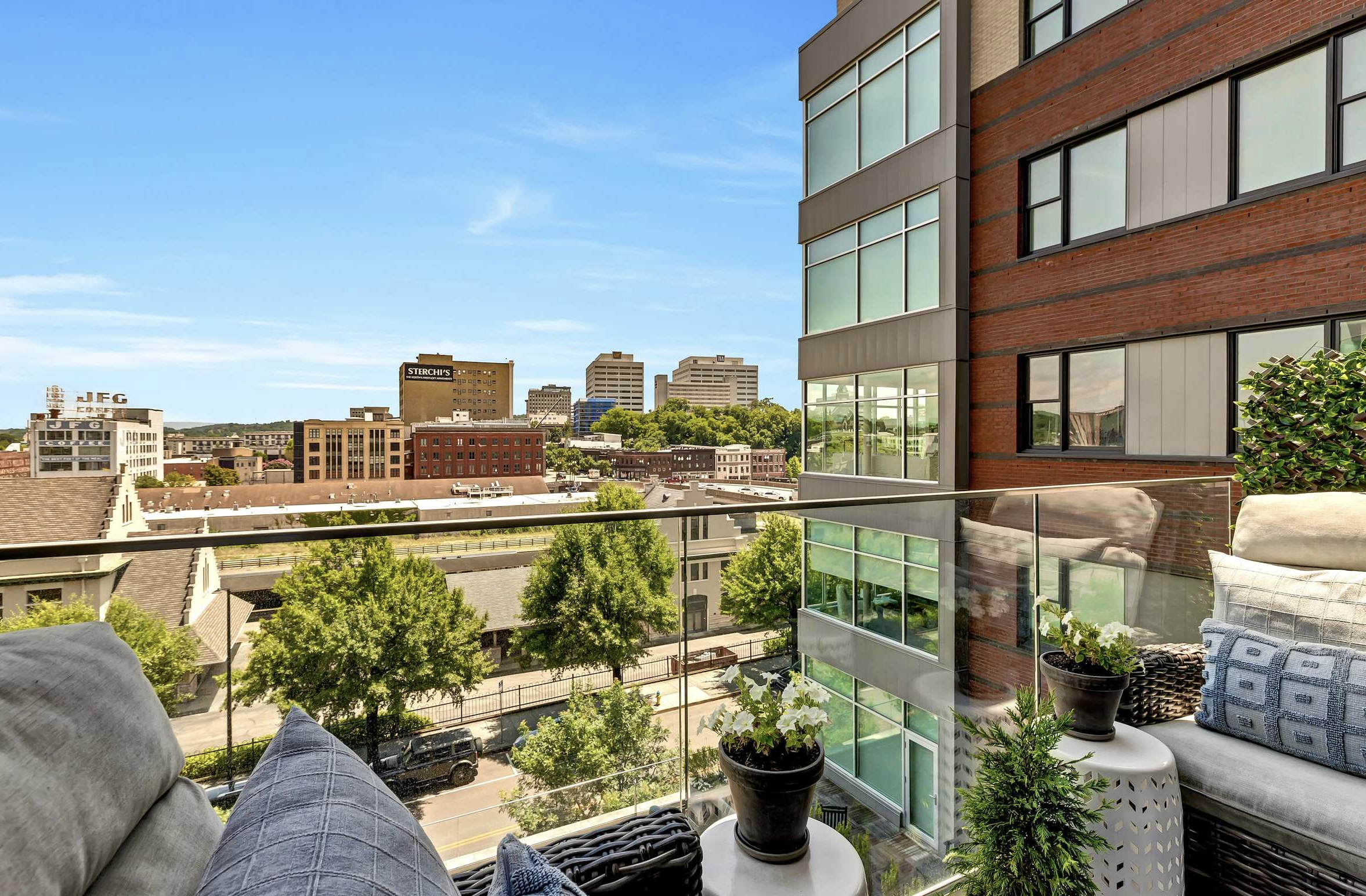 Balcony view of city skyline with buildings, trees, and blue sky.