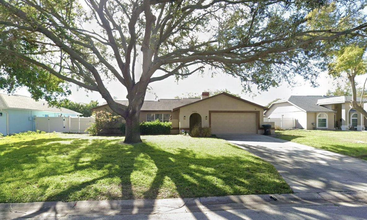 Front yard of a house with a large tree casting shadows on the grass and driveway.
