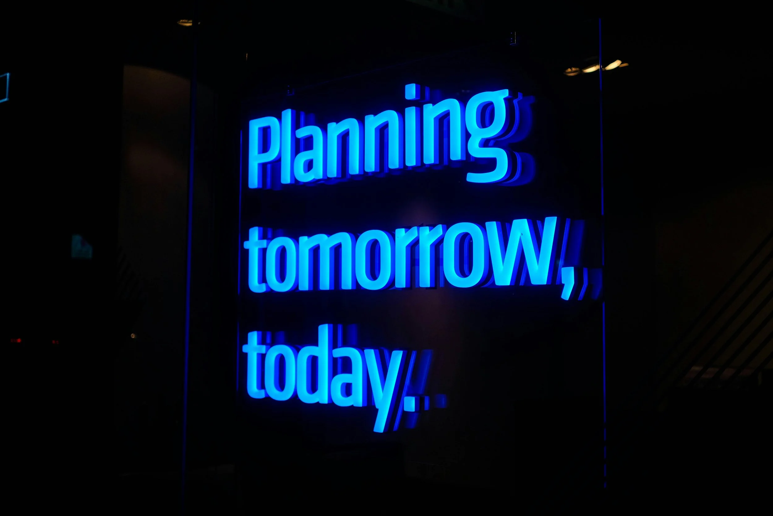Bright blue neon sign that says 'Planning' on top and 'today' on the bottom, reflected on a black surface.