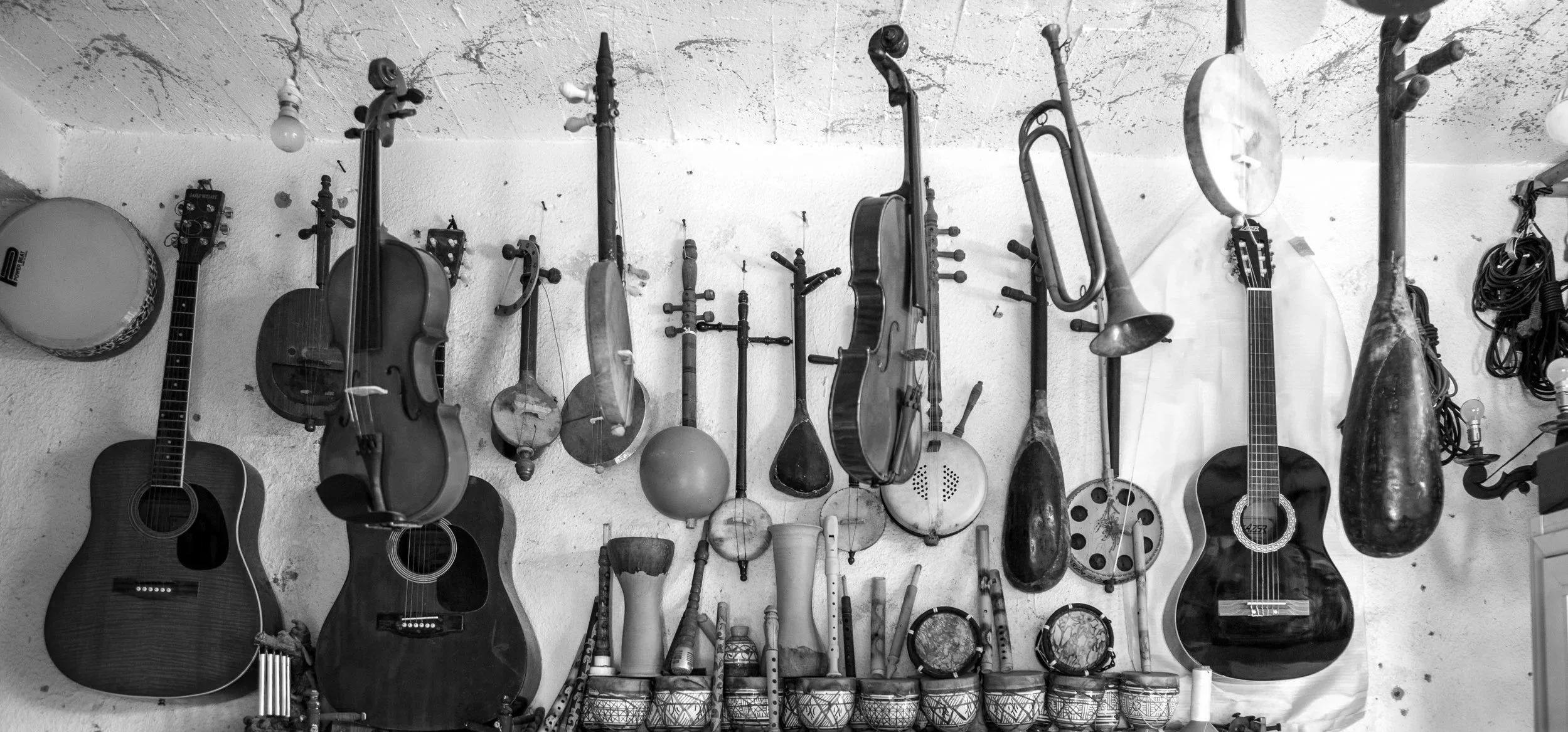 Collection of guitars, violins, and percussion instruments hanging on a wall in a music room