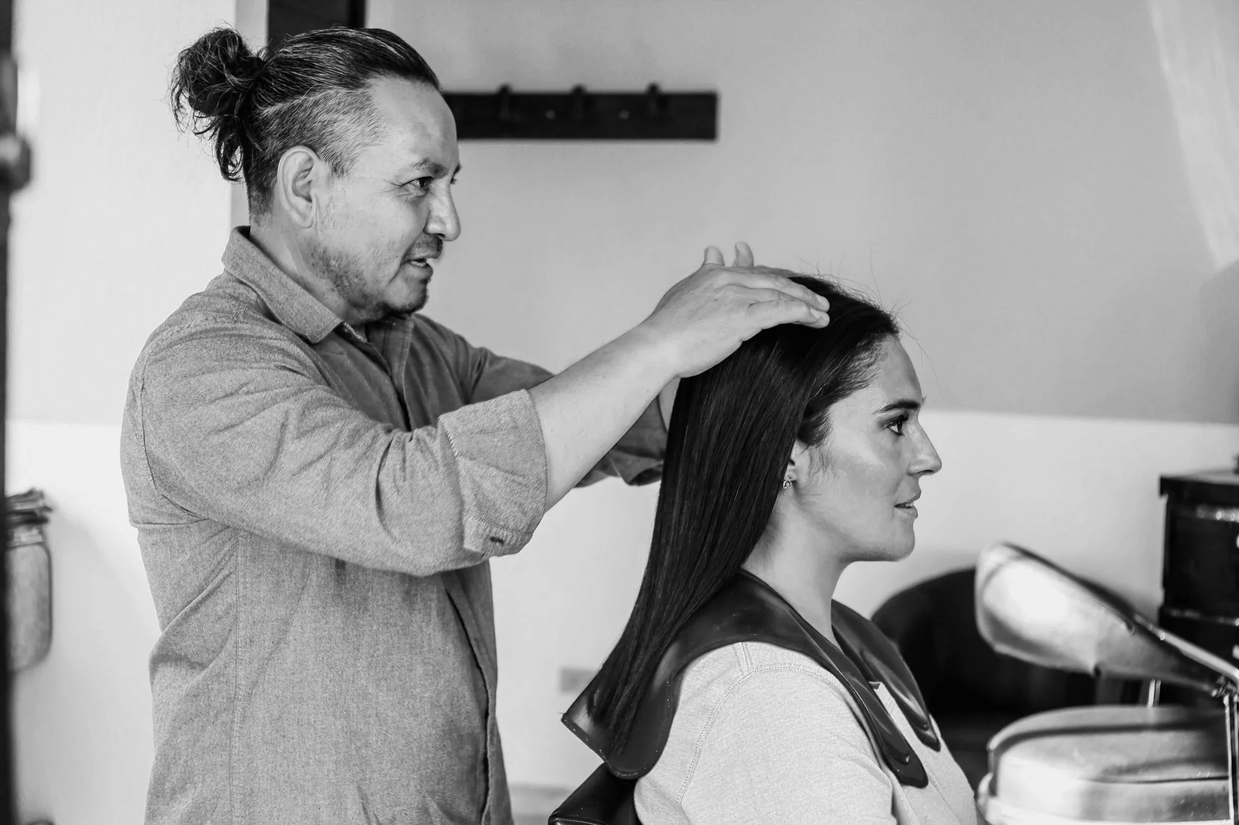 A hairstylist arranging a woman's long, straight hair in a salon with a mirror and styling tools in the background.