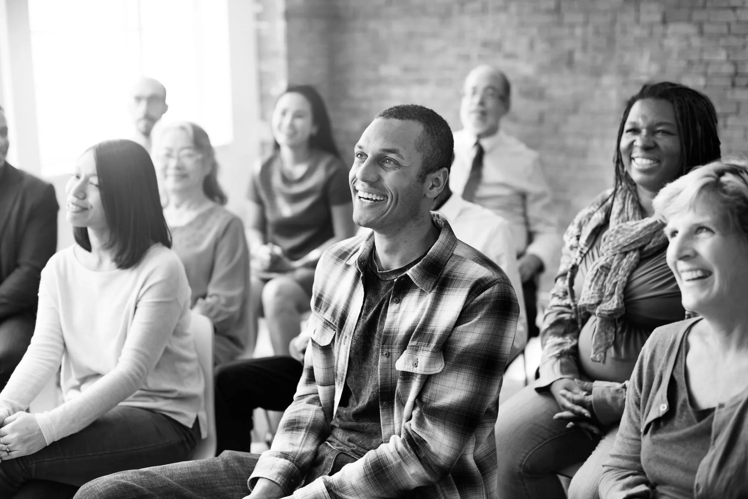 A diverse group of people sitting and smiling during a presentation or seminar in an industrial-style room.