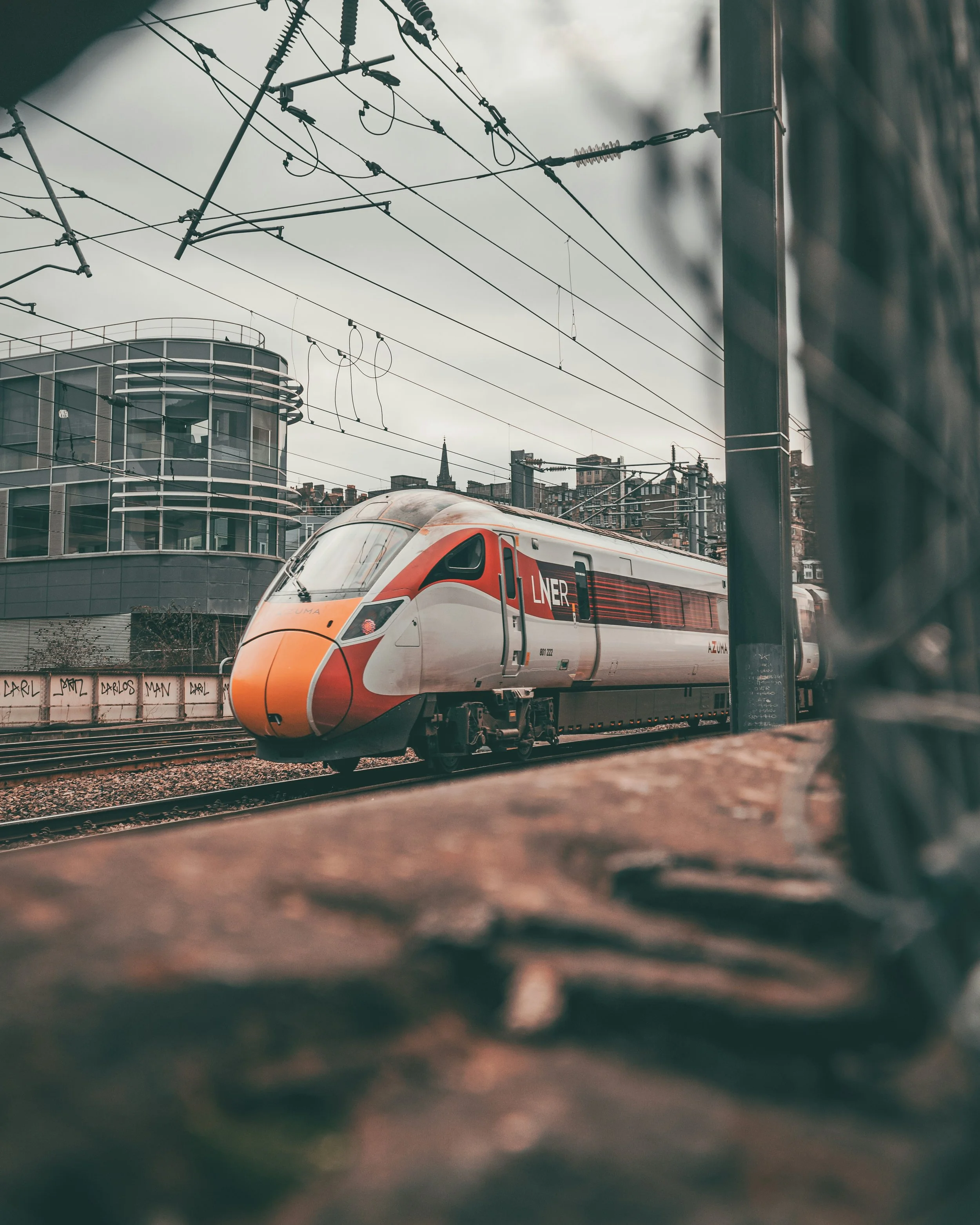 High-speed train arriving at a train station with city buildings and overhead electric wires.