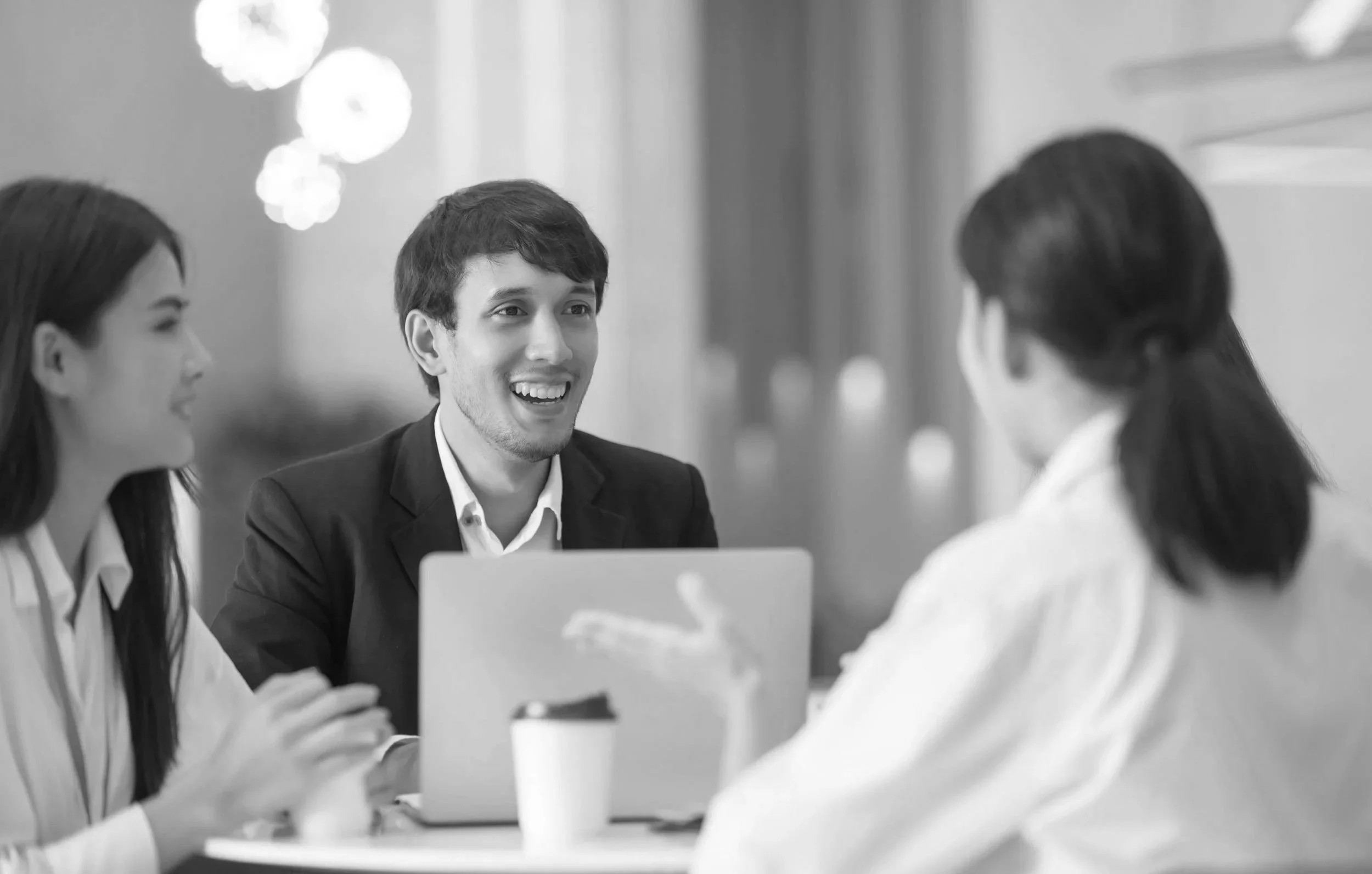 Three people engaged in a conversation in a professional setting, with a laptop and coffee mug on the table.