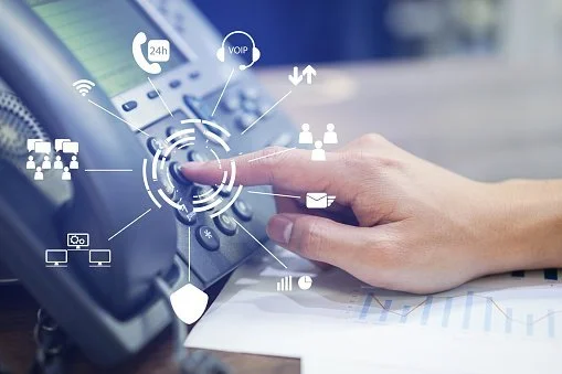 Close-up of a person's hand pressing a button on a business phone with digital icons of communication and technology surrounding it.