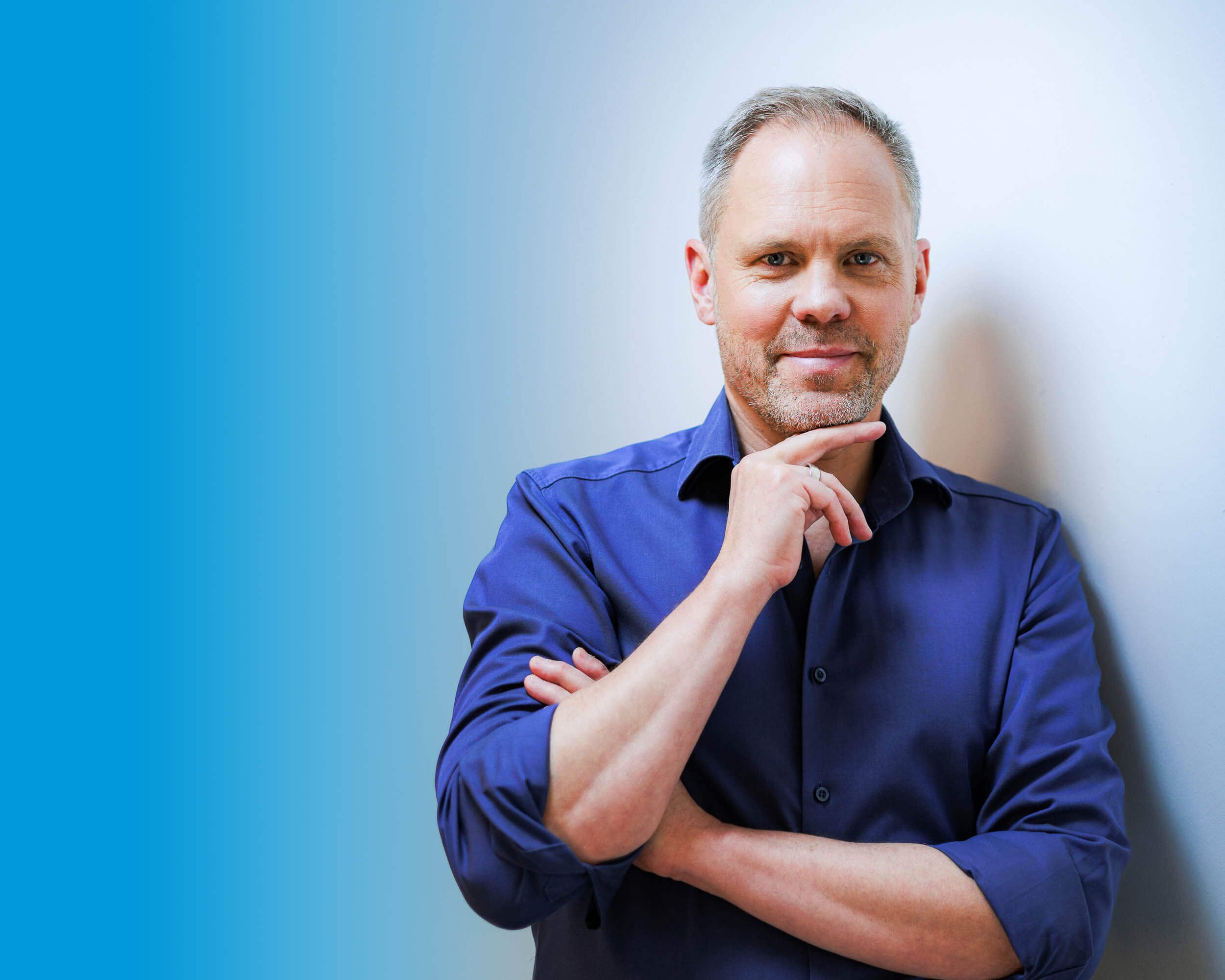 Businessfotograf Berlin: Thomas Dürst im blauen Hemd mit Hand am Kinn vor Studiohintergrund