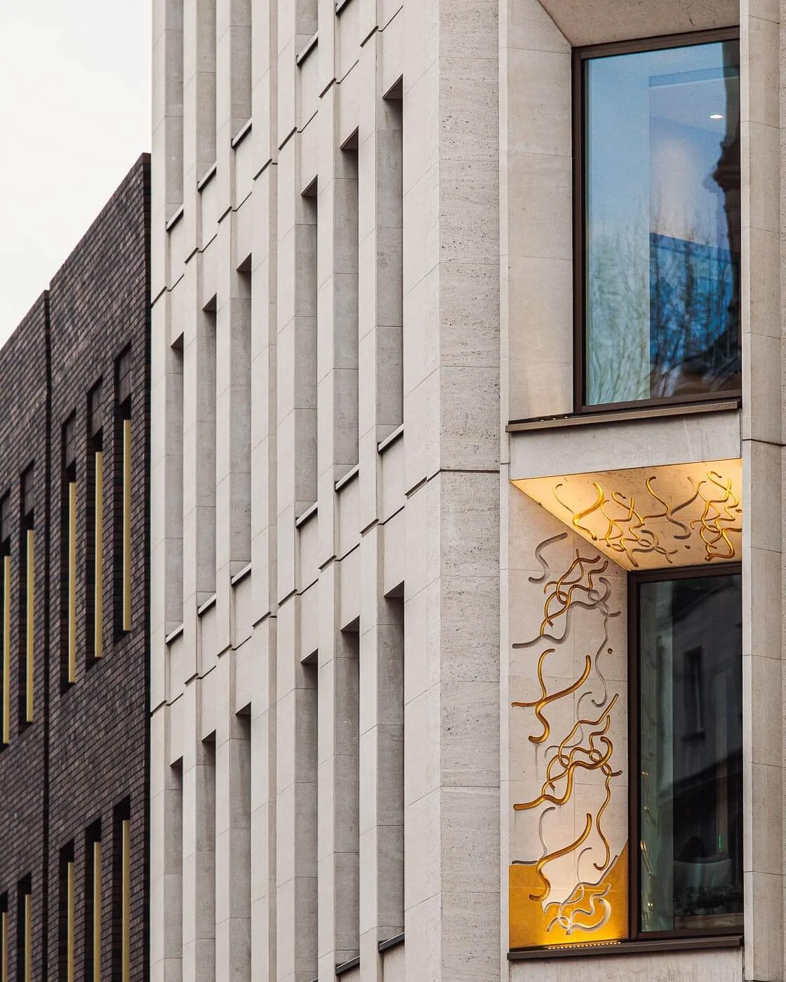 Architekturfotograf Berlin: Natursteinfassade in London mit vertikaler Lisenengliederung und goldfarbenem Wandrelief in beleuchteter Eingangsnische