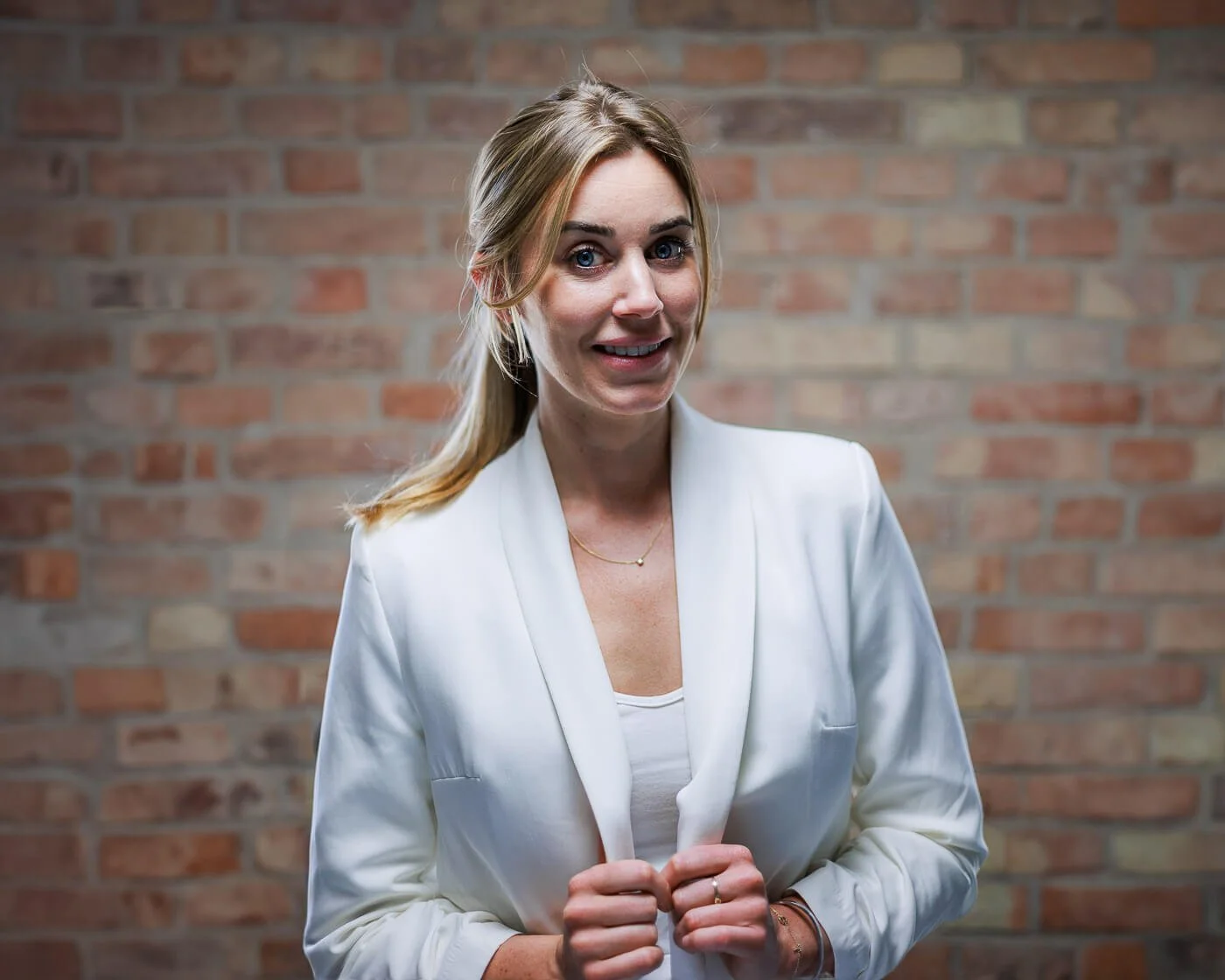 Businessfotograf Berlin: Beatrice Frensel im weißen Blazer lächelnd vor einer Backsteinwand