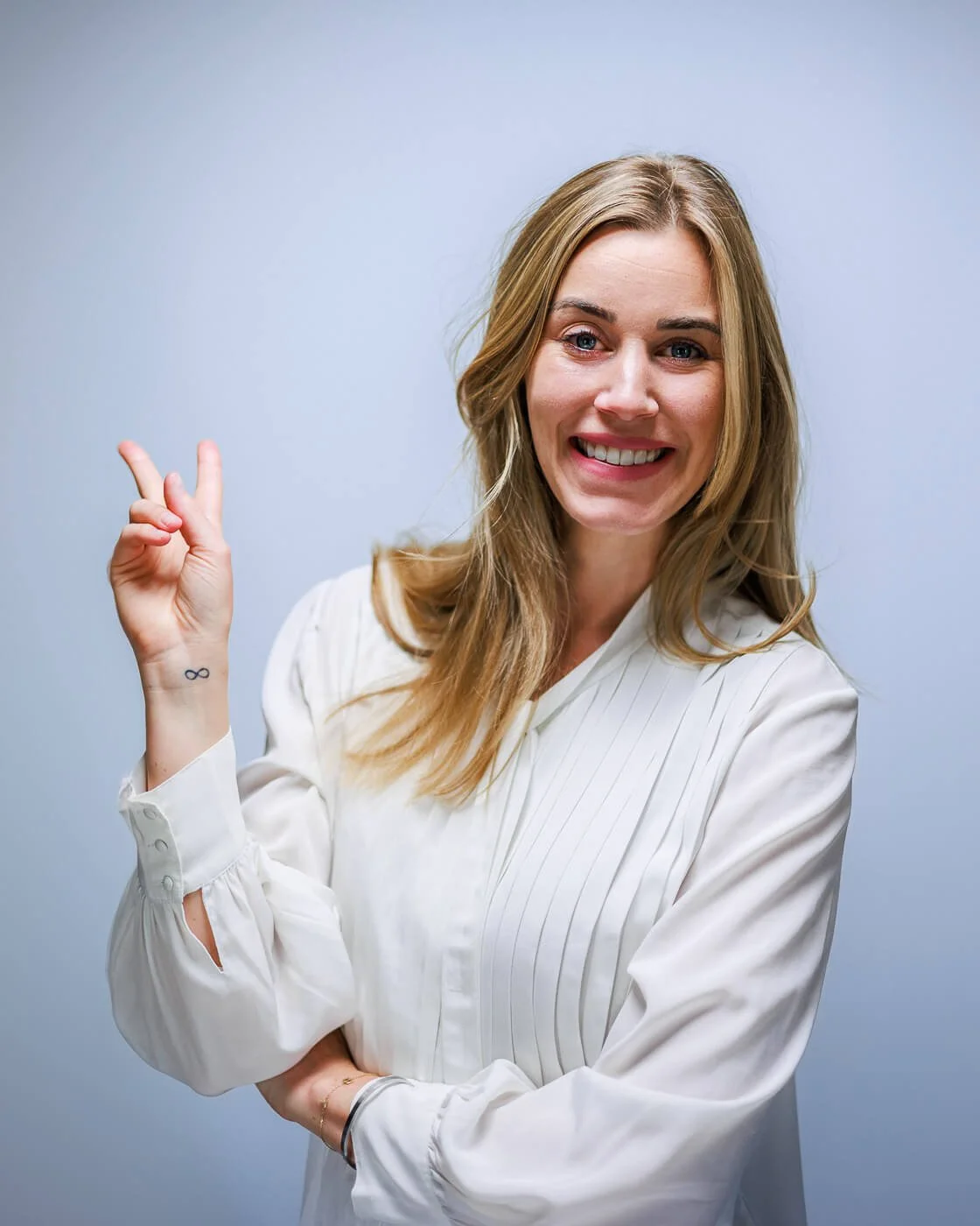 Businessfotograf Berlin: Businessporträt von Beatrice Frensel in weißer Bluse mit Handgeste vor grauem Studiohintergrund