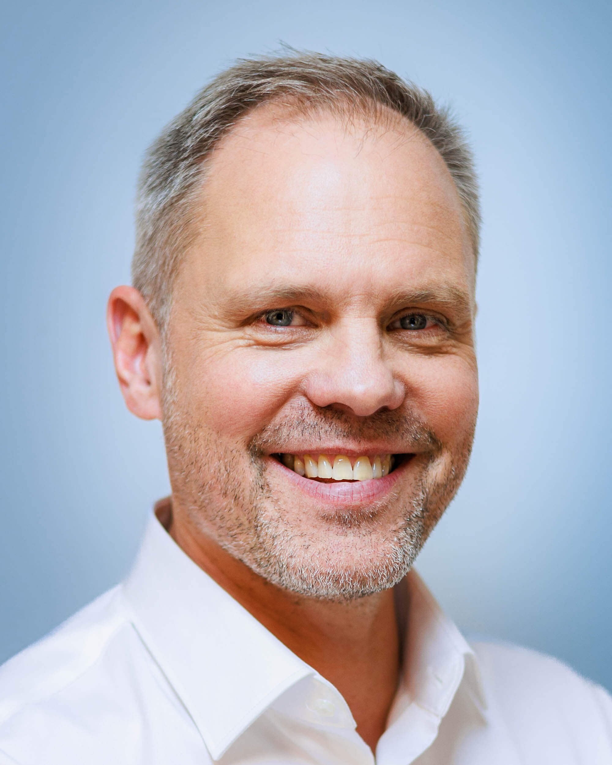 Businessfotograf Berlin: Headshot von Thomas Dürst lachend vor blauem Studiohintergrund