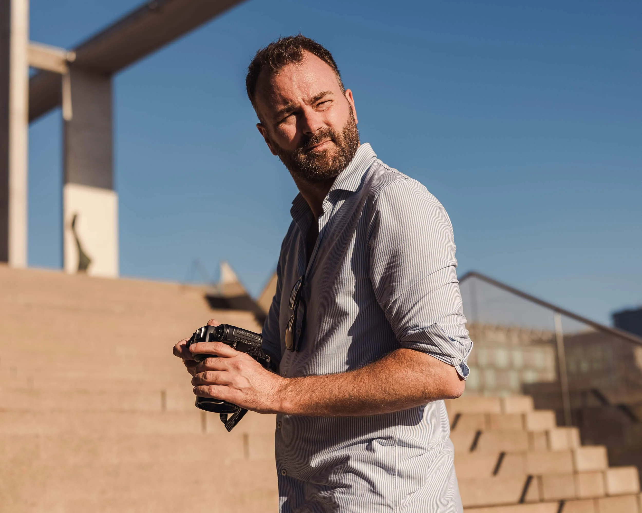Businessfotograf Berlin: Porträt von Maximilian von Alvensleben mit Kamera auf einer Freitreppe vor Sichtbetonarchitektur
