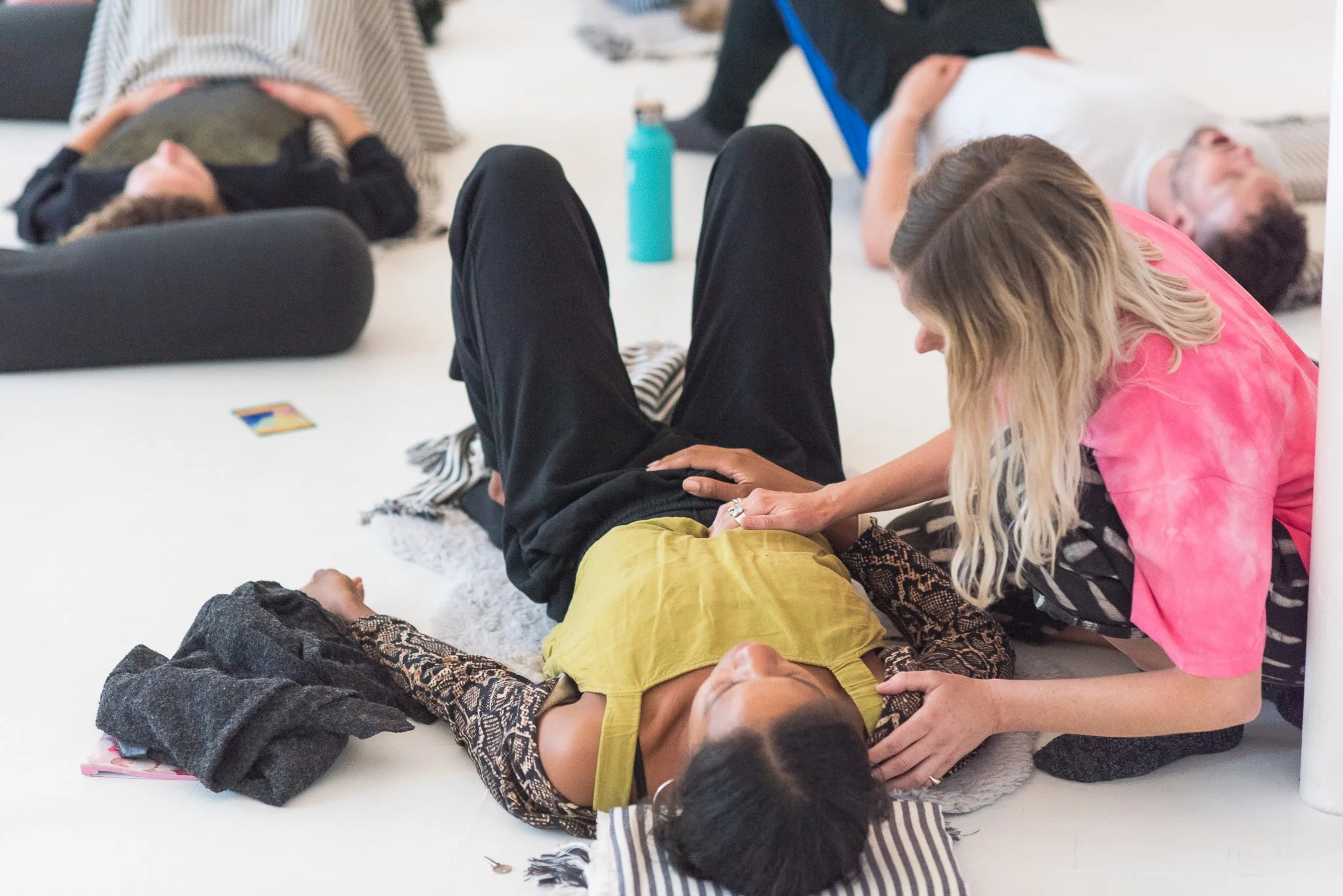A woman lies of the floor practising Transformational Breath and being facilitated with acupressure points by Brenna Duncan of Arise Breathwork