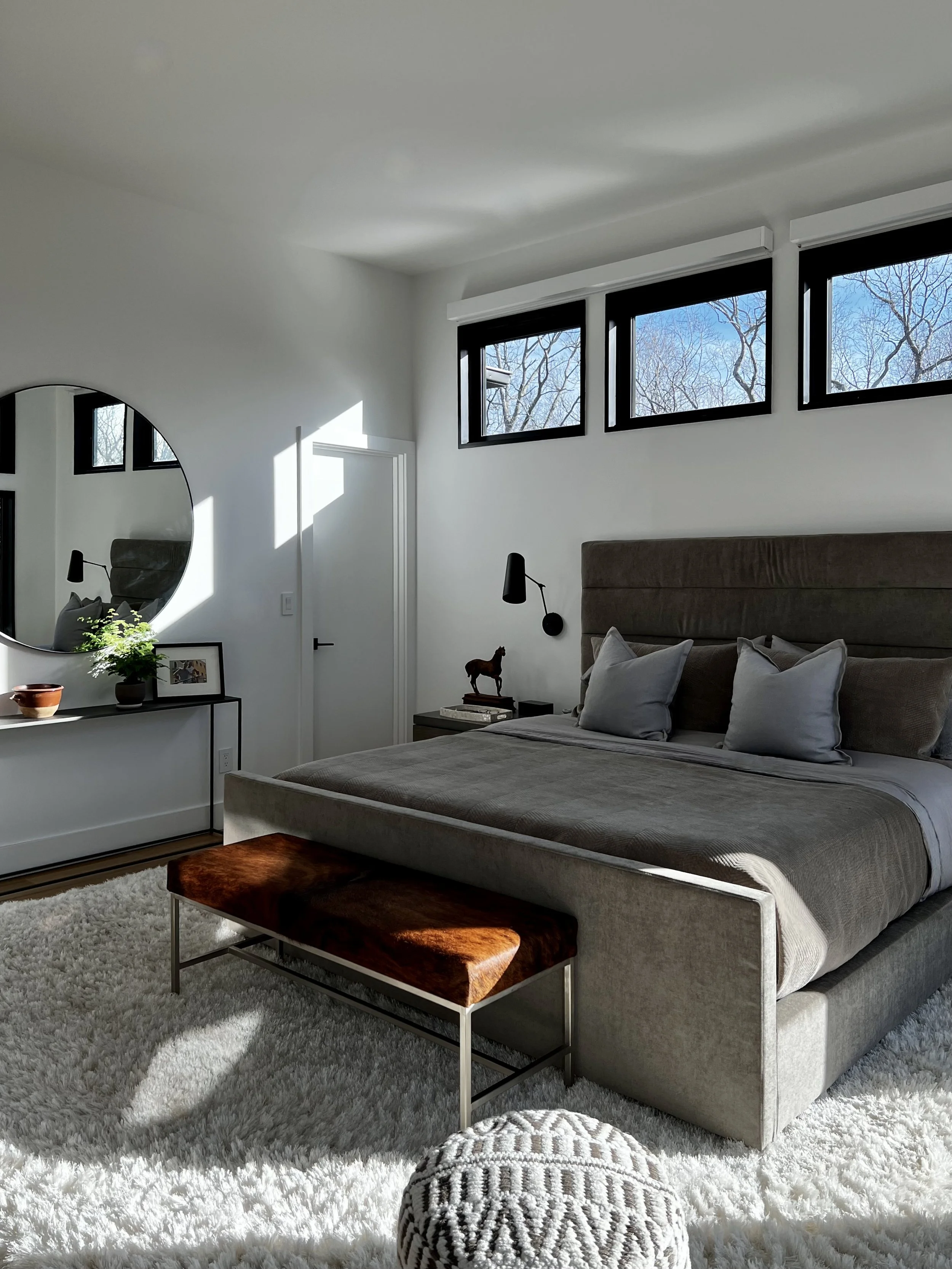 Serene primary bedroom with upholstered bed, neutral textiles, clerestory windows, and minimalist furnishings filled with natural light