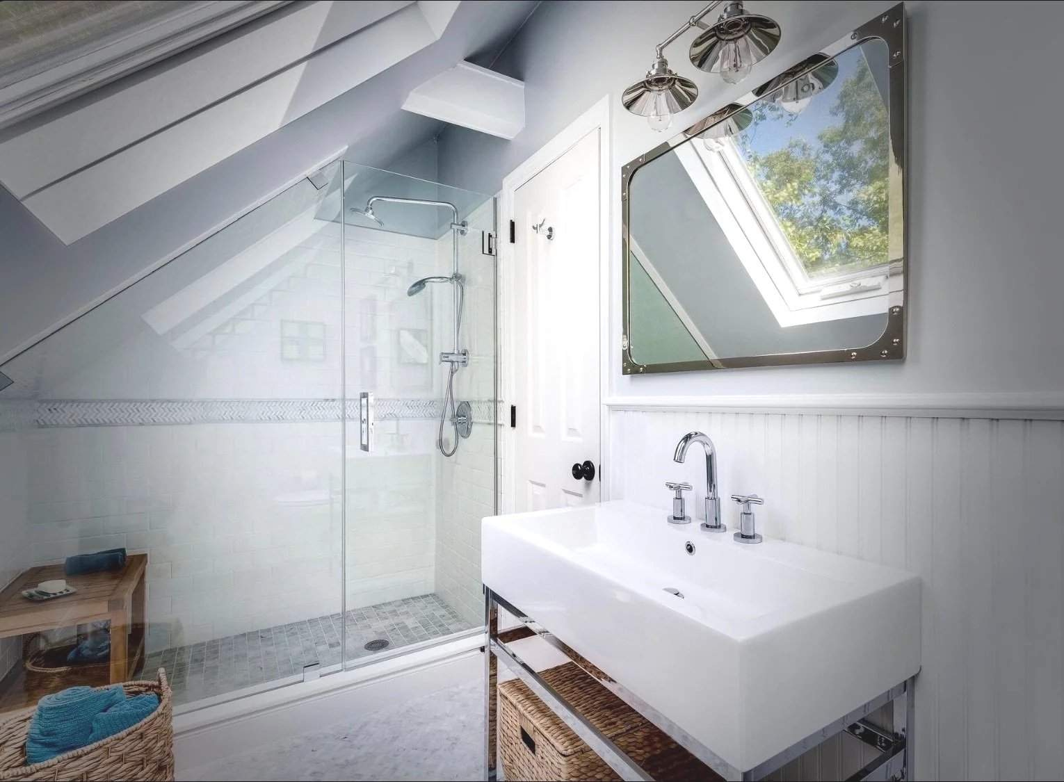 Bright bathroom with a sloped ceiling, glass shower enclosure, white tile walls, a white sink with a mirror and natural light from a skylight window.