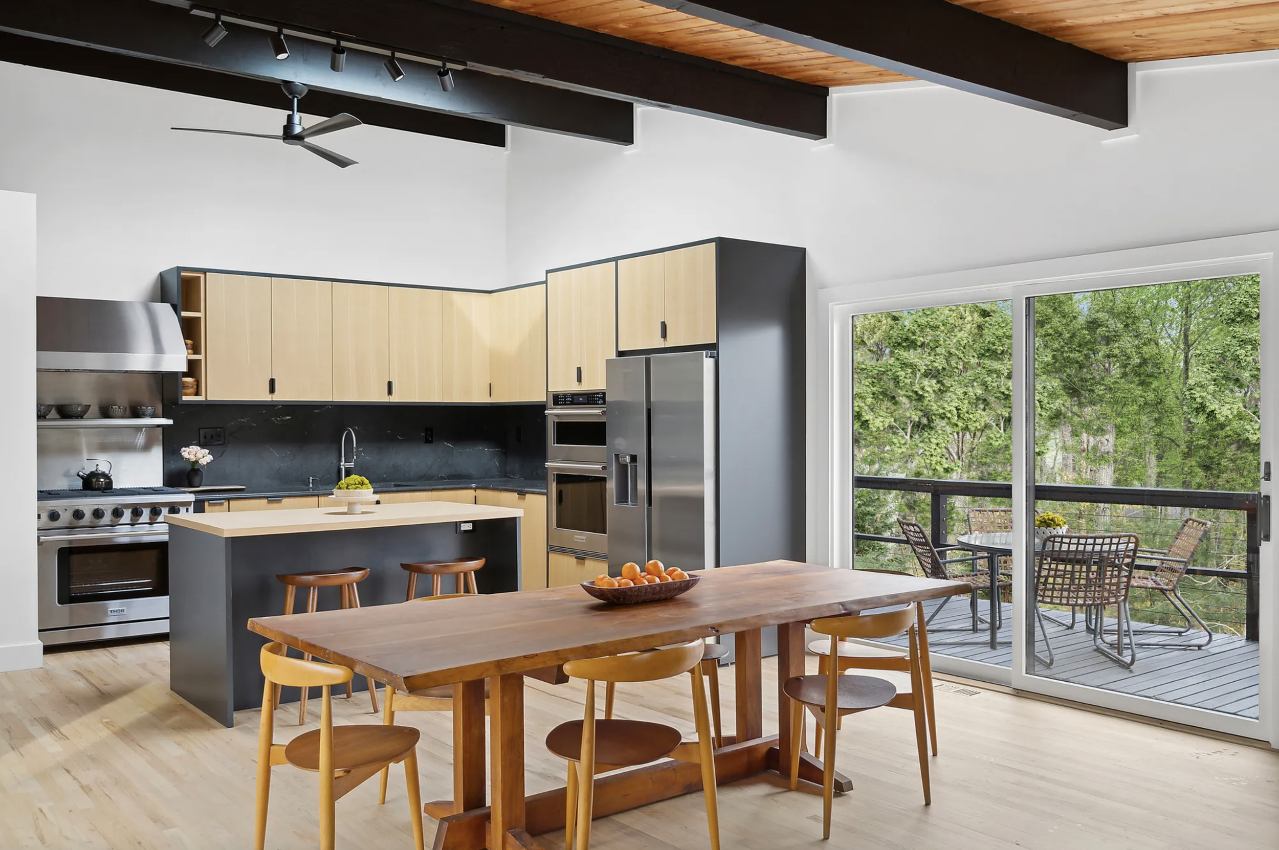 Open kitchen and dining space with light wood cabinetry, central island, solid wood dining table, and sliding glass doors overlooking trees