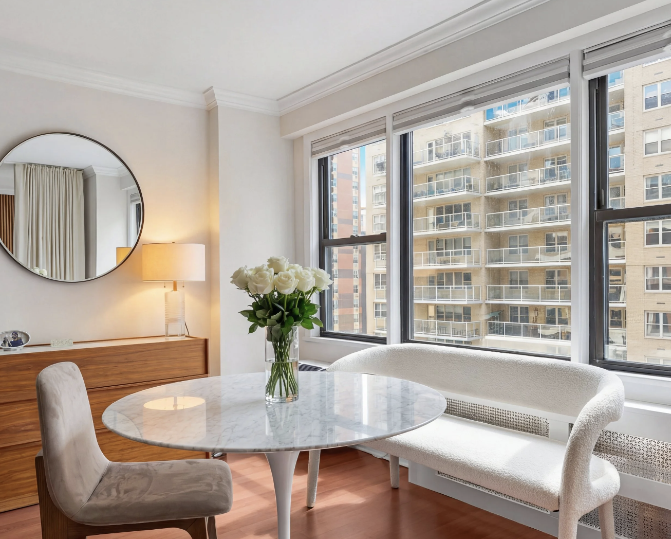 Bright NYC condo dining area with round marble table and floor-to-ceiling windows.