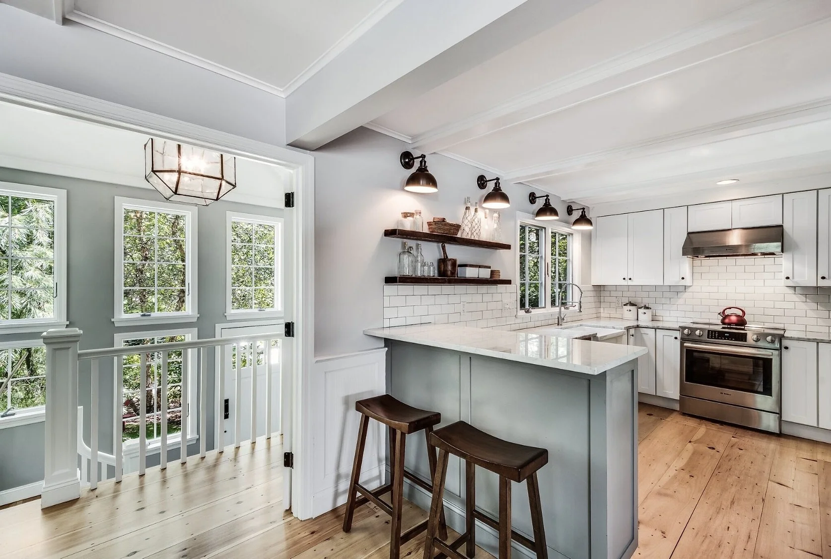 Bright, classic kitchen with white cabinetry, subway tile backsplash, a pale gray island with wood stools, and large windows bringing in natural light