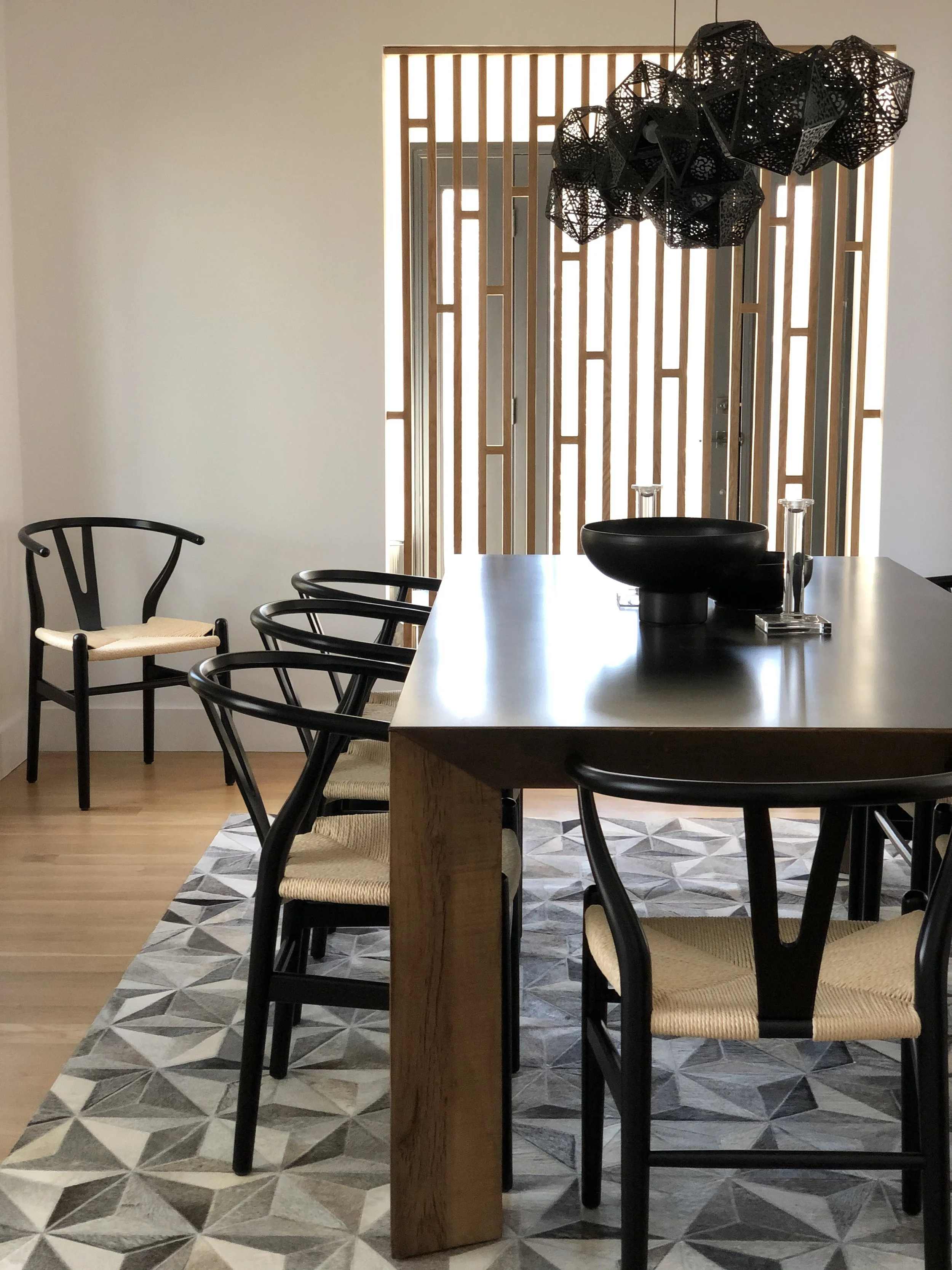 Dining room with a solid wood table, black sculptural chairs, geometric rug, and statement pendant framed by a wood screen