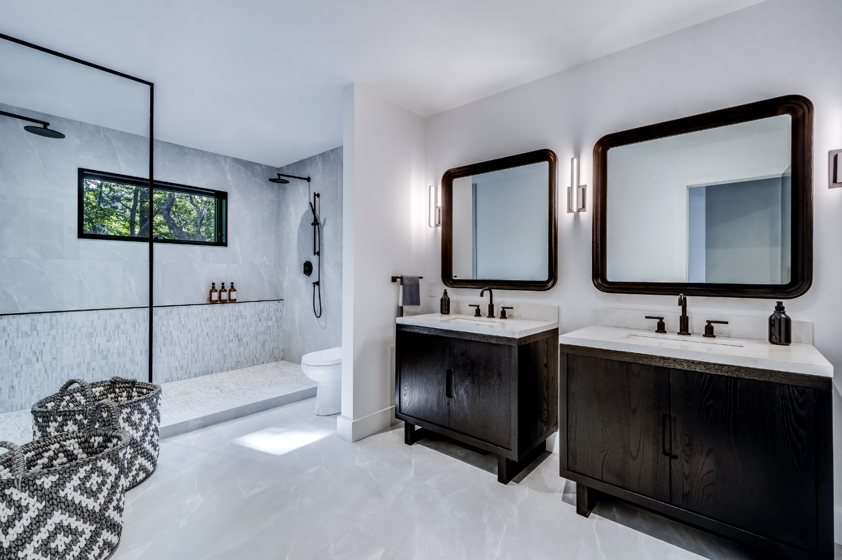 Minimal bathroom featuring a walk-in shower, double vanity with dark wood cabinets, sculptural mirrors, and polished stone floors